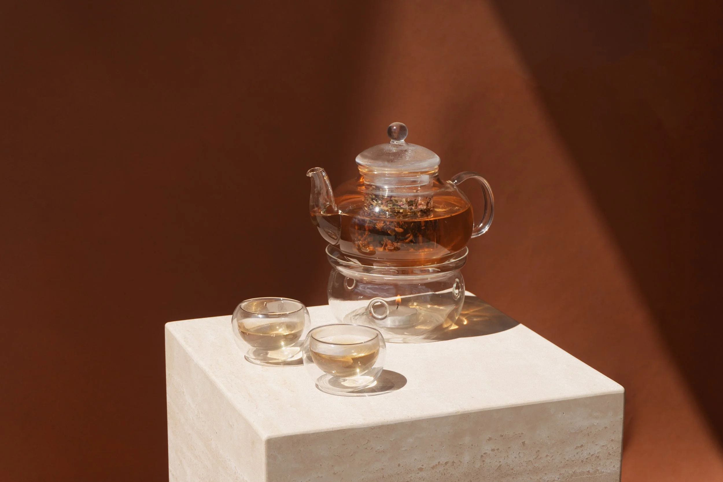 Glass teapot with tea and two cups on a stone pedestal.