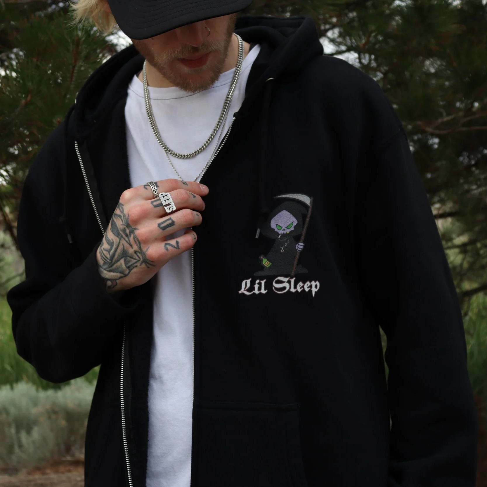 Black Zip Up Hoodie With the Lil Sleep Sleepy Reaper design on the front and a back picture of the sleepy reaper in a back alley with sleep garffiti on the wall and a burning trash can and a logo that says sleep now die later under the picture