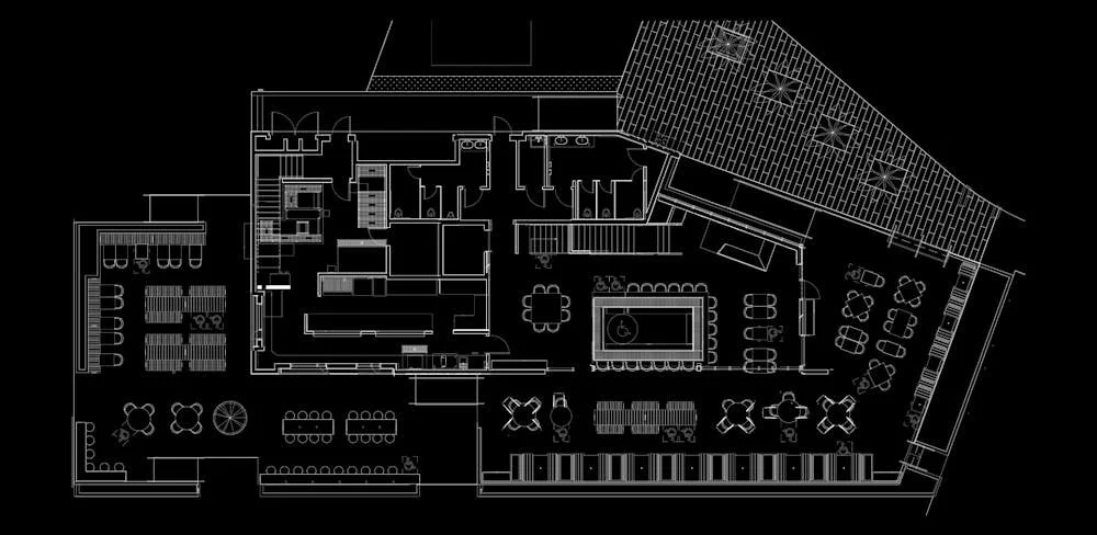 Architectural floor plan of a commercial space with various seating areas and tables, a bar or counter, restrooms, and distinct sections for dining and gathering. The design includes structured layouts and partitions.