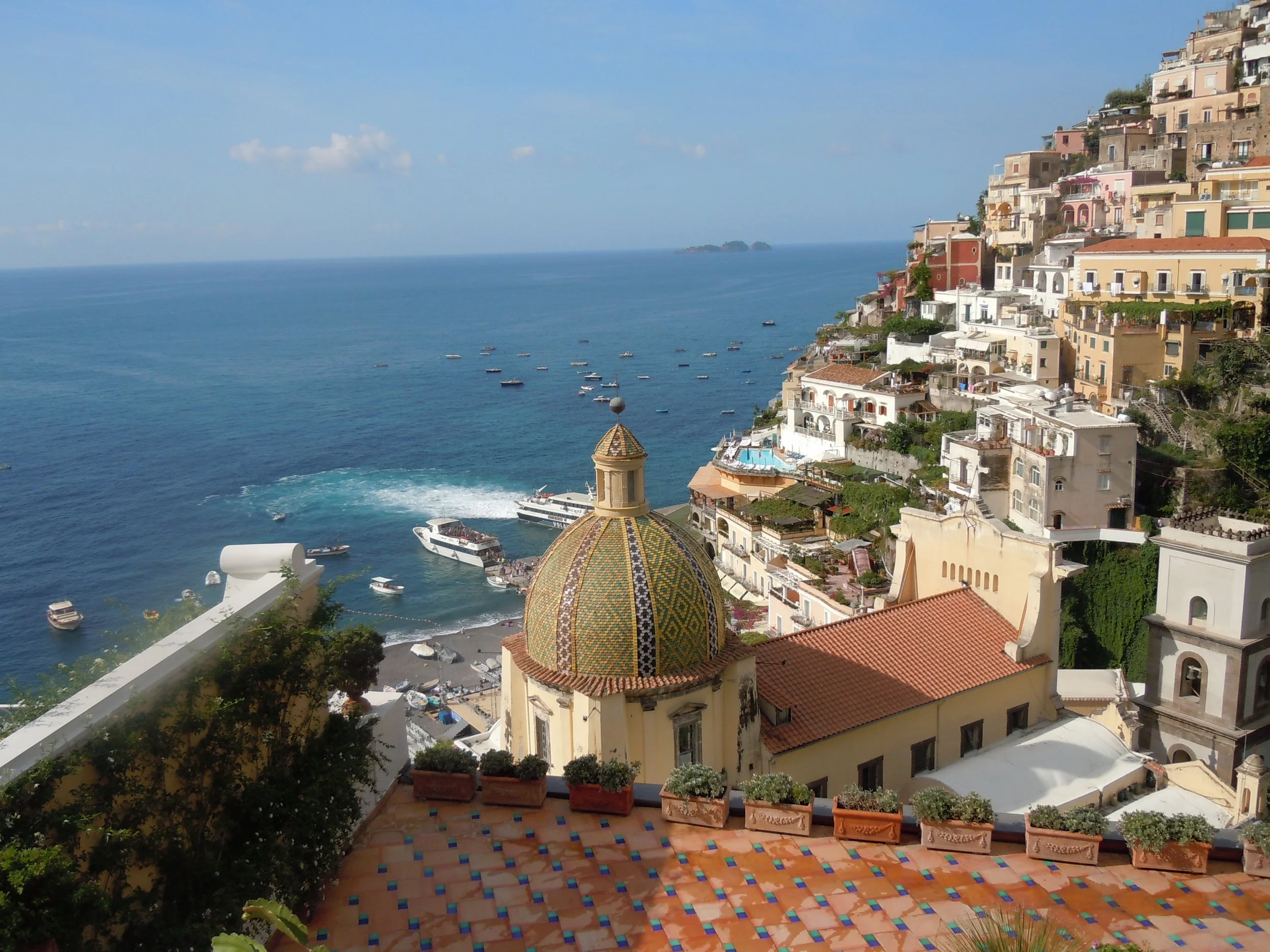Scenic view of Positano, Italy with colorful cliffside houses, a dome church, and boats on the blue sea in Amalfi Coast, Italy.
