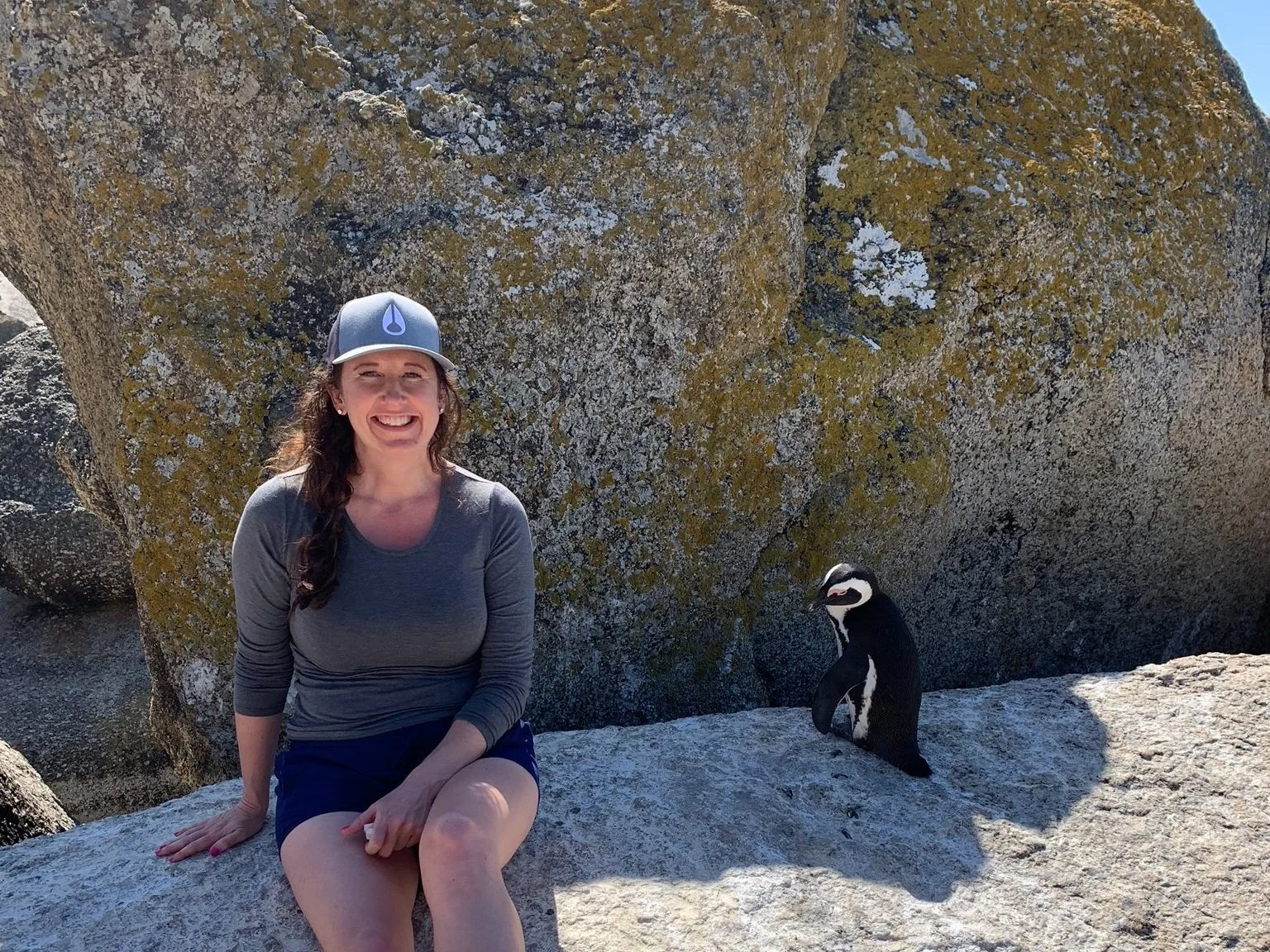 Woman sitting on rocks at Boulders Beach in South Africa is connecting with a penguin.