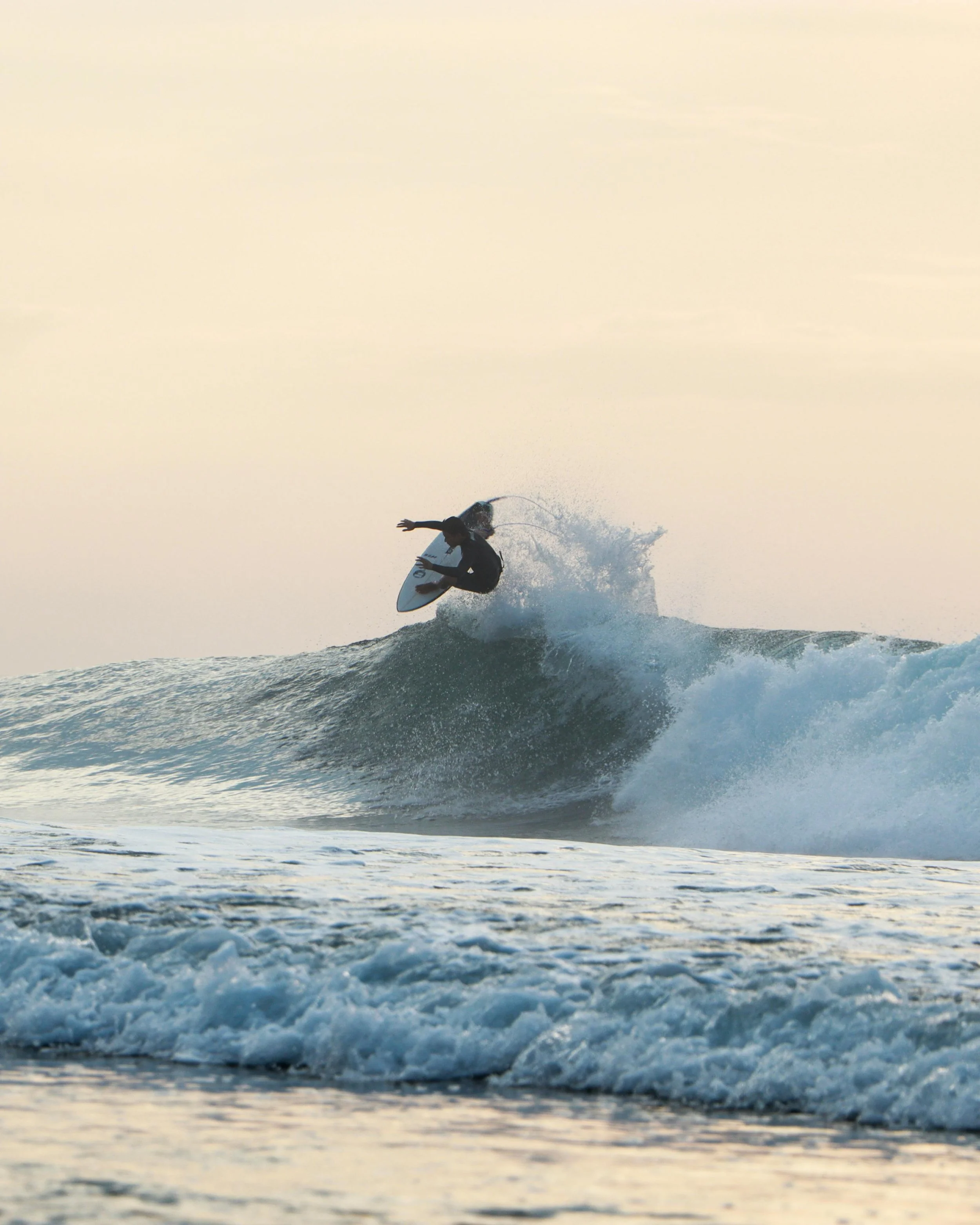 A person surfing on a wave during sunset at the beach.