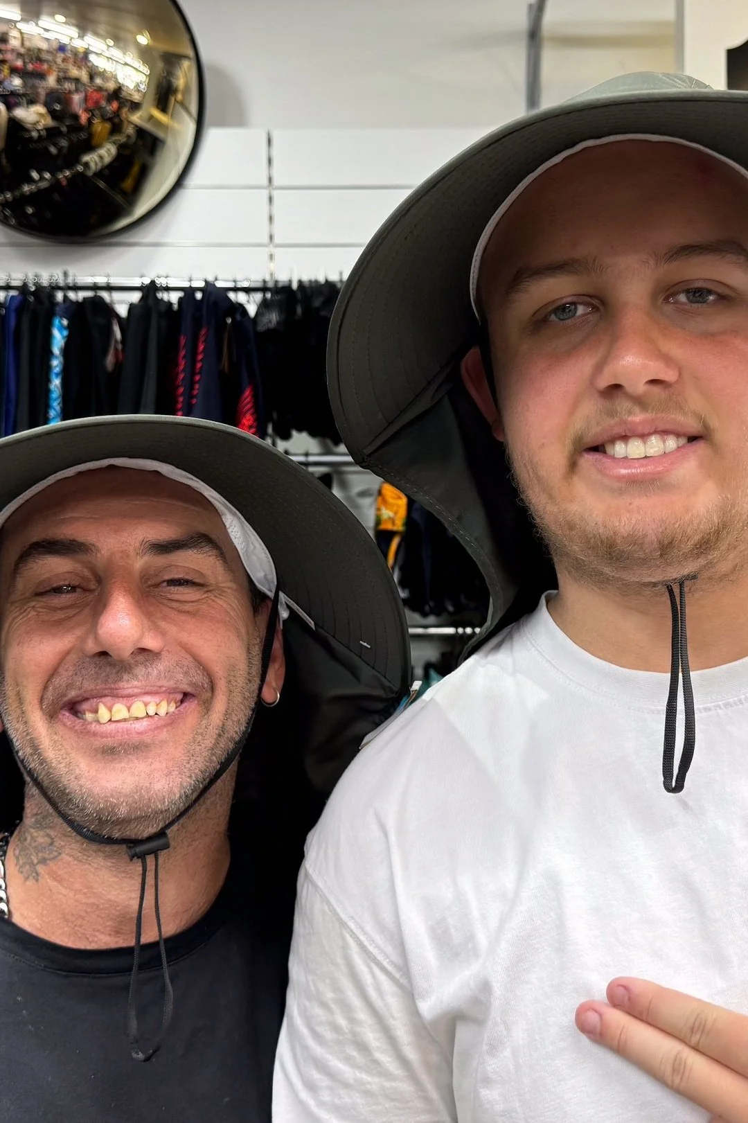 Two men wearing outdoor hats in a store, with clothing racks and accessories visible in the background.
