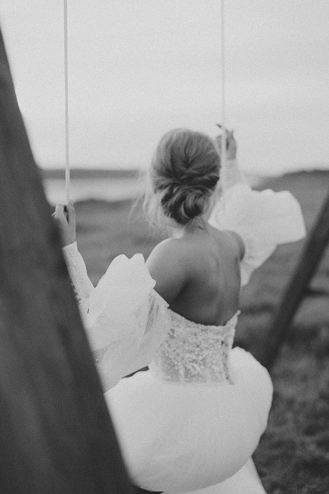 Black and white photo of a woman in a wedding dress on a swing