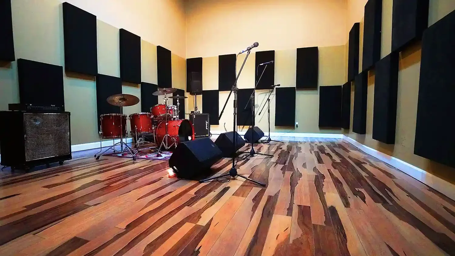 Salle de pratique avec batterie rouge, hauts-parleurs, microphones, amplificateurs et panneaux acoustiques