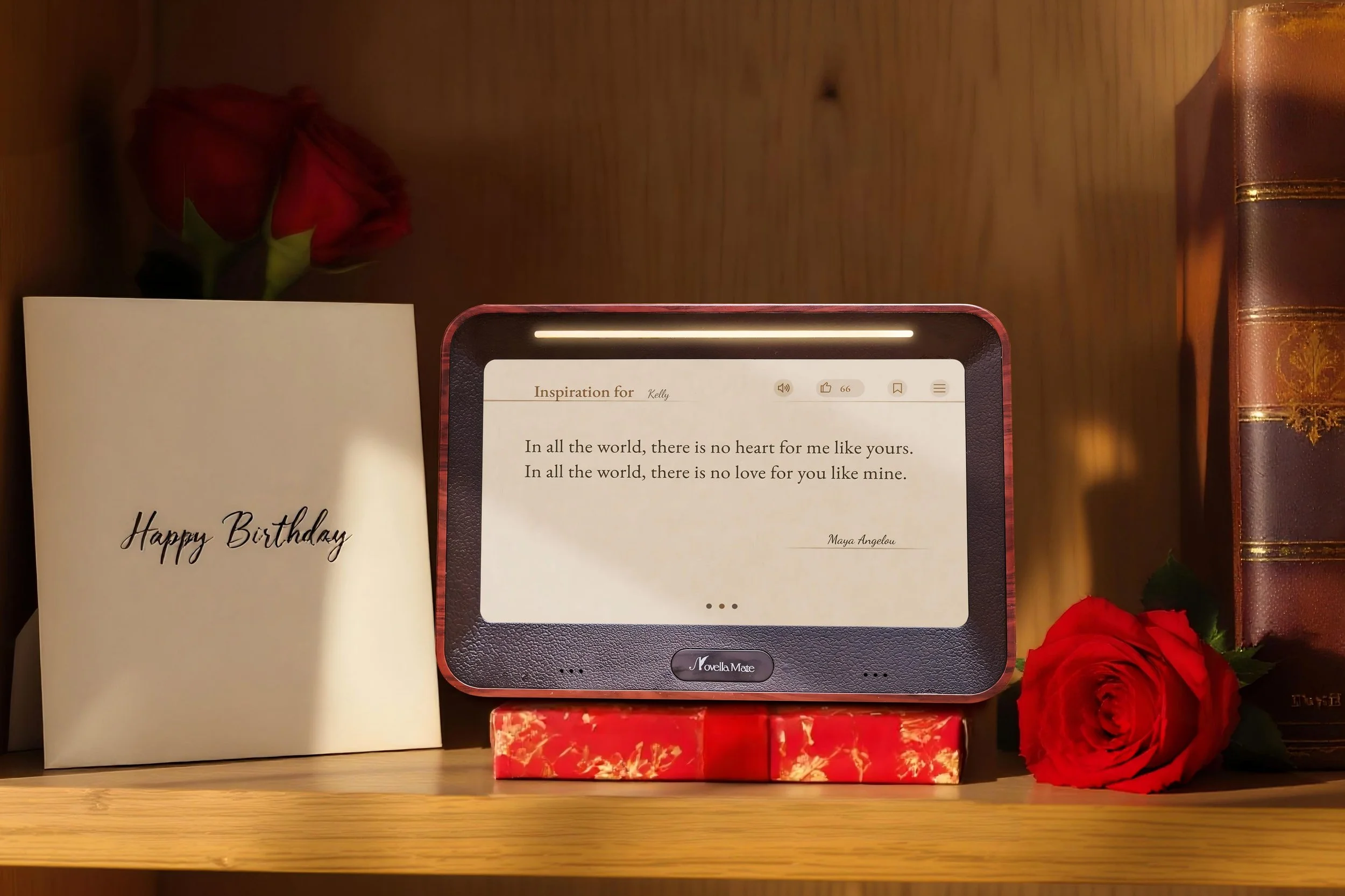 NovellaMate, a literary clock, the best gift for book lovers. A birthday card with 'Happy Birthday' written on it, a small digital device with a quote from Maya Angelou, a red rose, and some books on a wooden shelf.