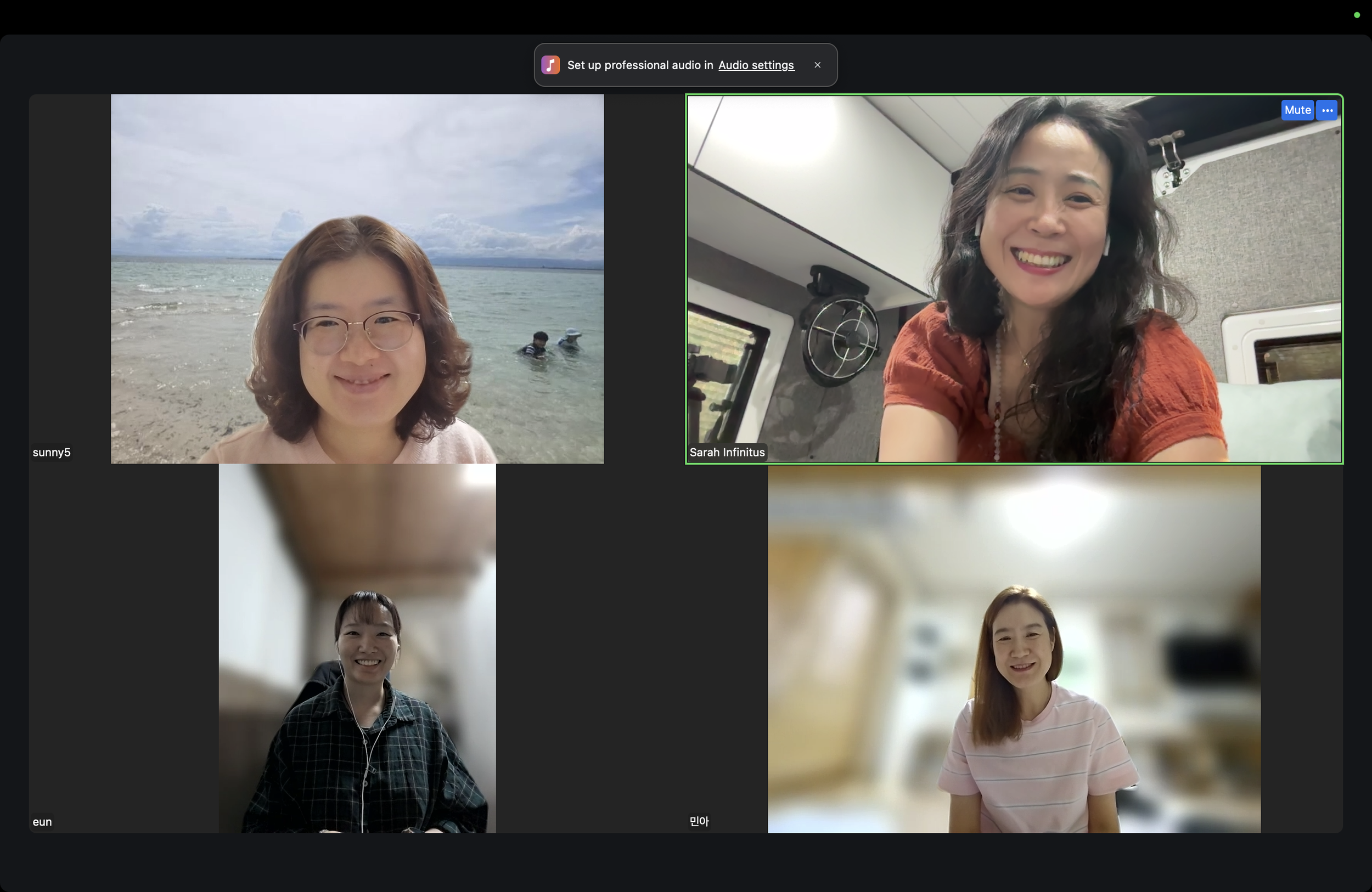 A screenshot of a video call showing six women smiling and looking at their cameras. The women are in different locations, with some visible backgrounds including a beach, a room with a vent, and a plain indoor setting.