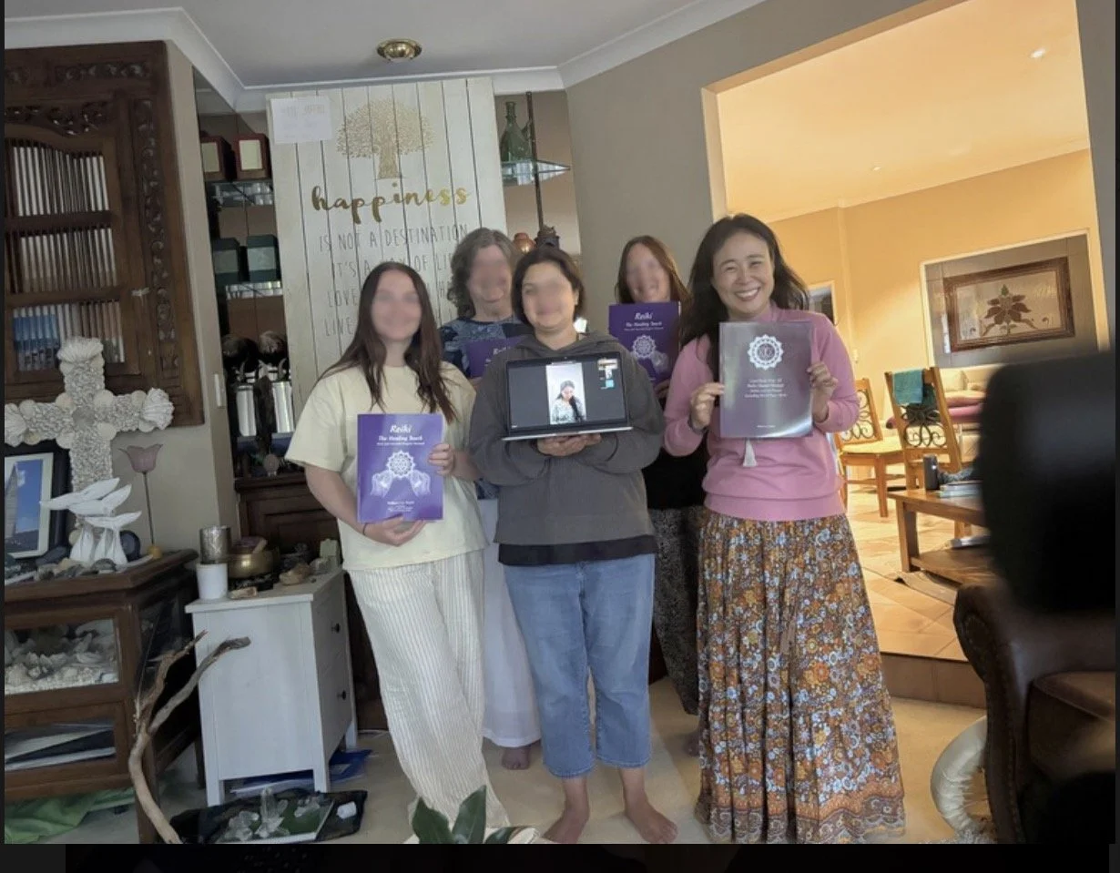 Group of six women standing inside a home, holding certificates and a tablet with a video call, smiling for the camera. Decor includes a cross and a sign that says 'happiness is not a destination...'