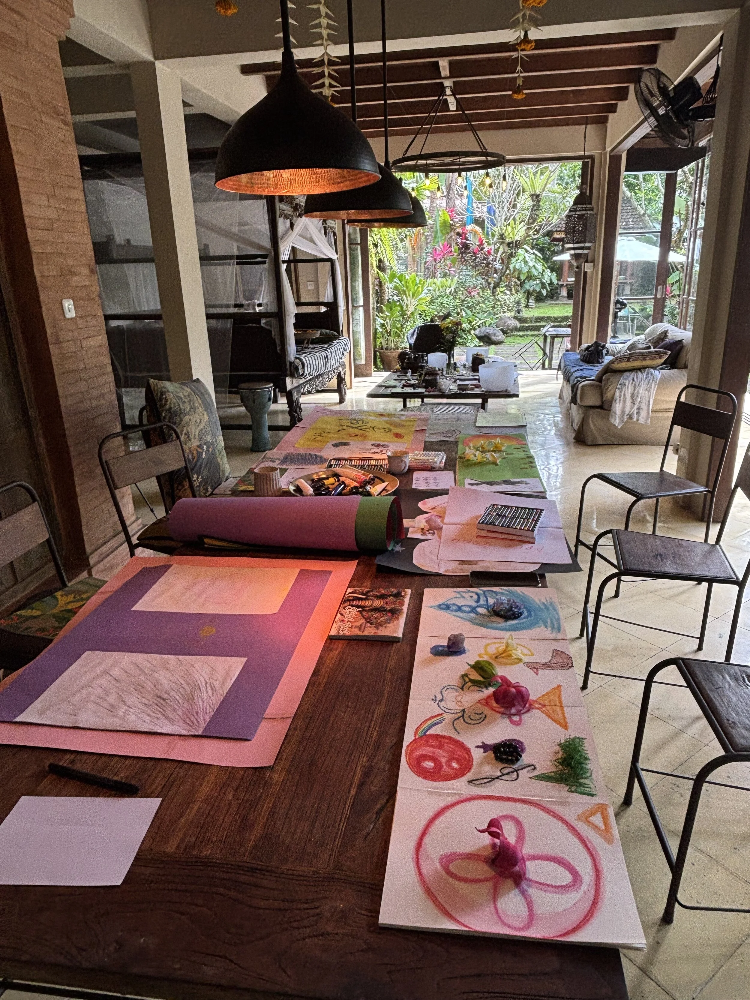 A dining table with various colorful drawings and paintings created by children, some featuring animals, flowers, and abstract shapes, spread out across the table surface.