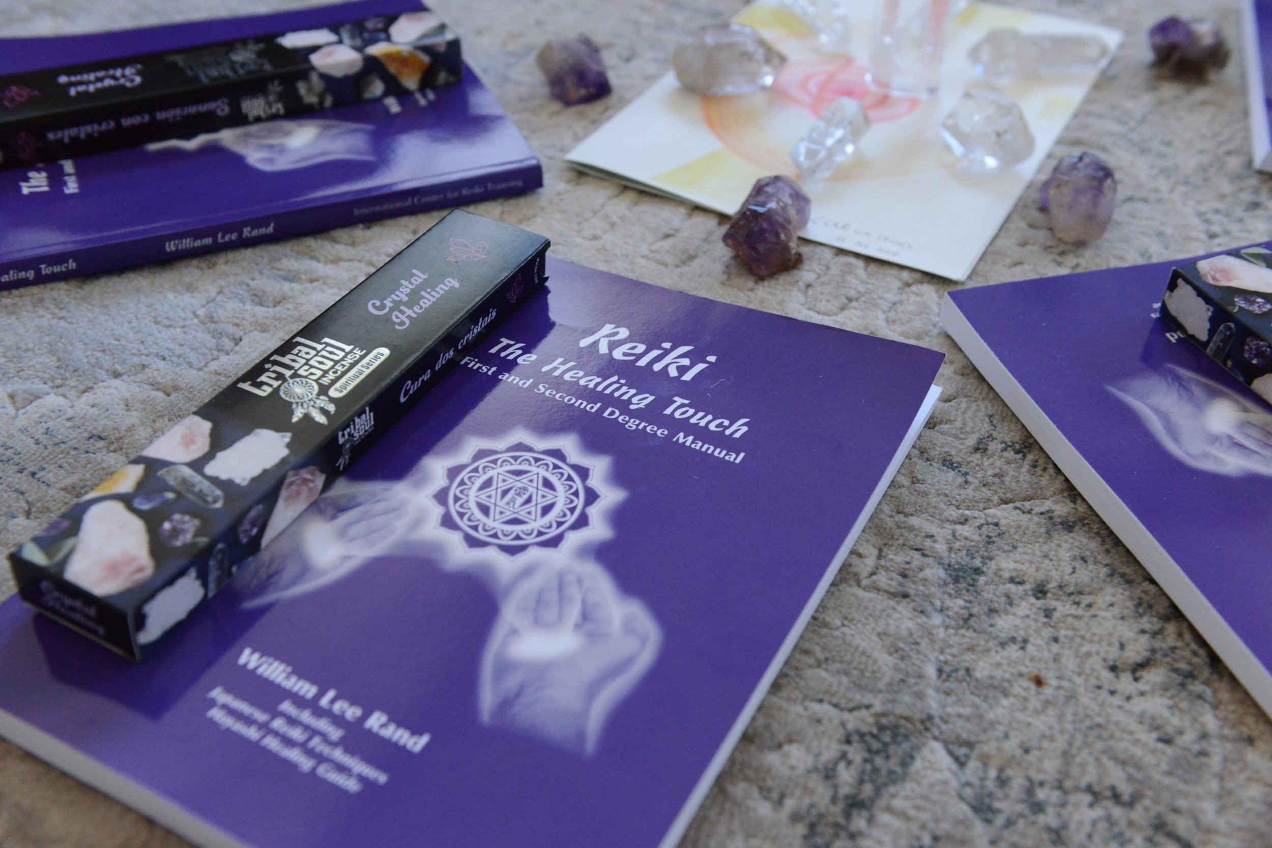 A collection of books, a box of crystals for healing, and loose crystals on a beige carpet.