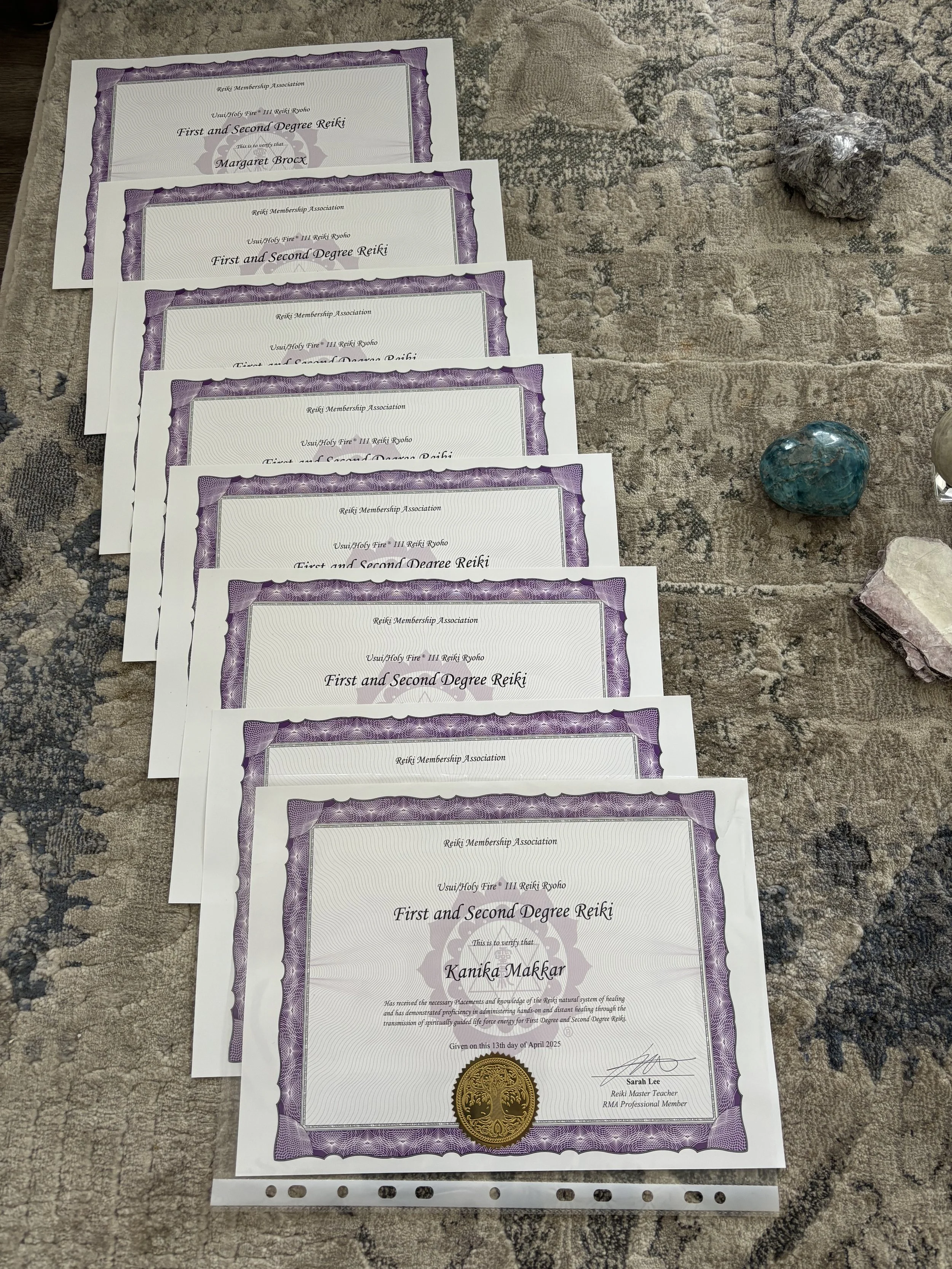 A series of certificates for First and Second Degree Reiki from the Usui Holy Fire III Reiki Ryoho Reiki Membership Association laid out on a patterned rug.