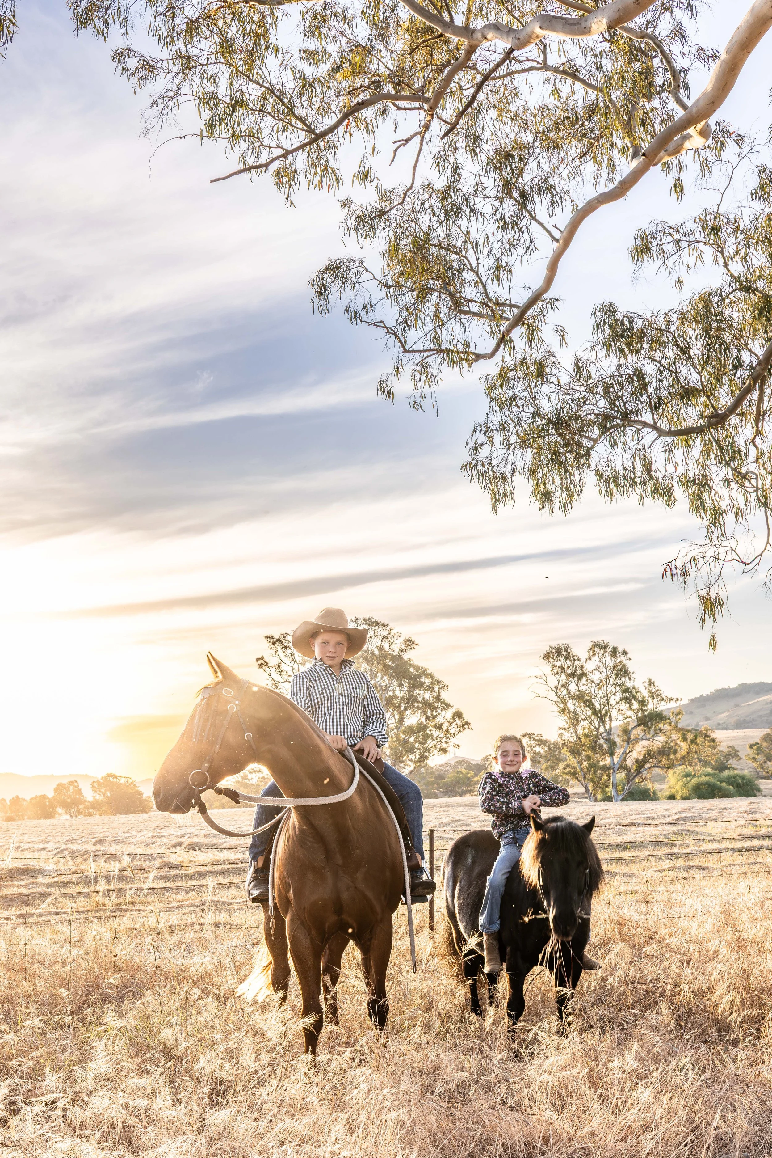 yong siblings sitting on their horses in the country at sunset