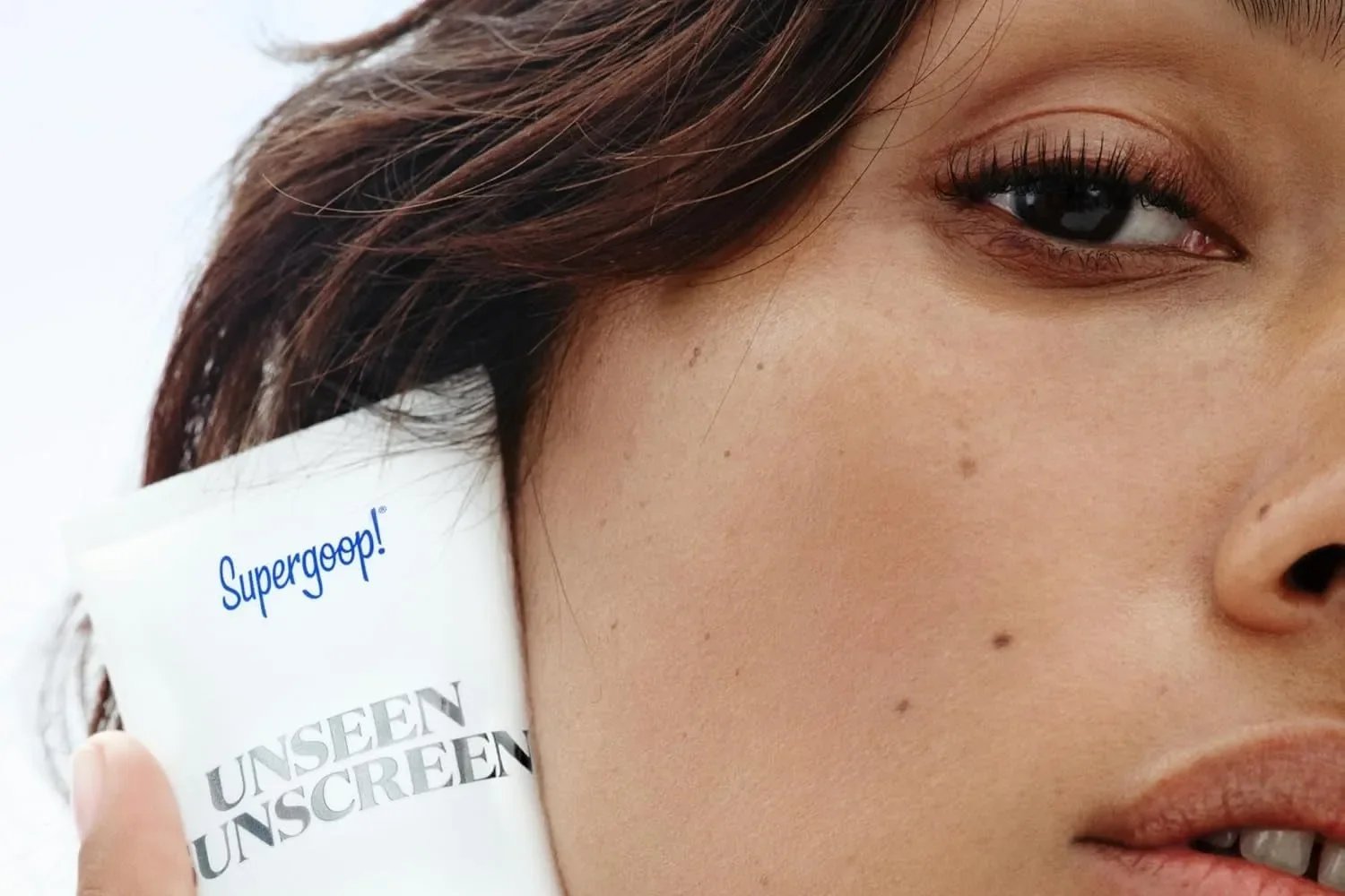 Model pressing a tube of Supergoop Unseen Sunscreen SPF 40 to her cheek, Supergoop campaign