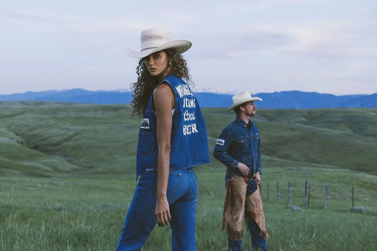 Wrangler denim on denim western look with a Coors graphic vest, white cowboy hats, and straight-leg jeans worn by two models in open ranch country at dusk, courtesy of Wrangler, featured in the SABLE WEST Bella Hadid style edit 2026