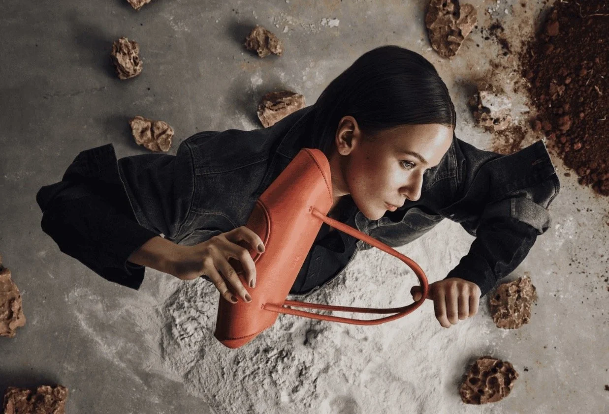 Model lying on plaster holding a coral behno leather shoulder bag, behno campaign