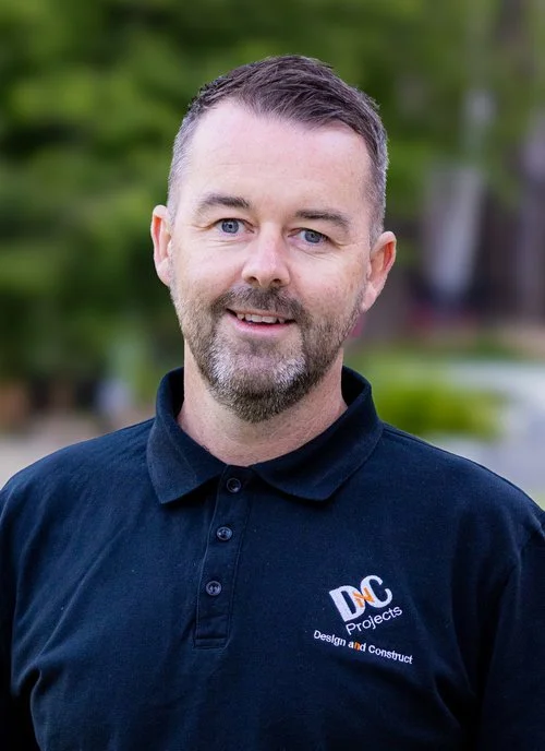 Man in a black polo shirt with "DOC Projects" logo standing outdoors, smiling at the camera.