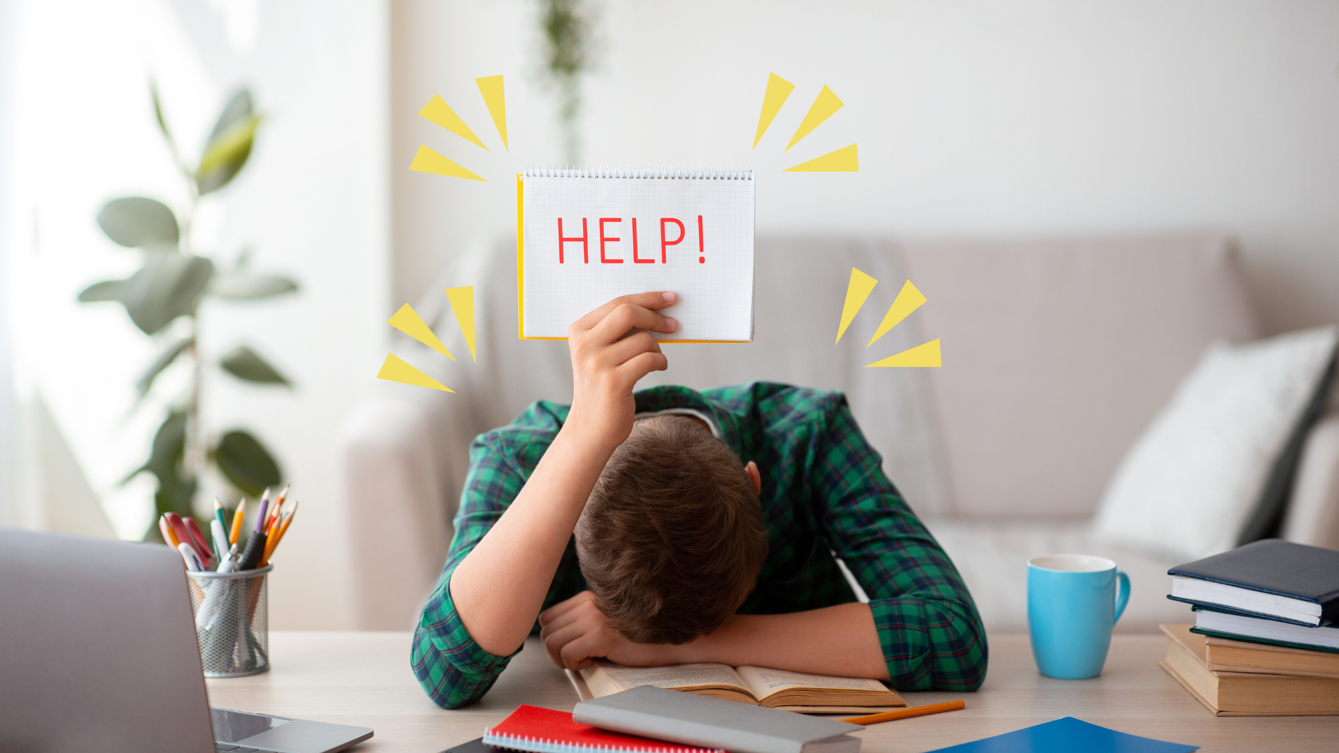 Person slumped over a desk holding a "HELP!" sign, with study materials and a laptop around them, indicating stress or frustration.