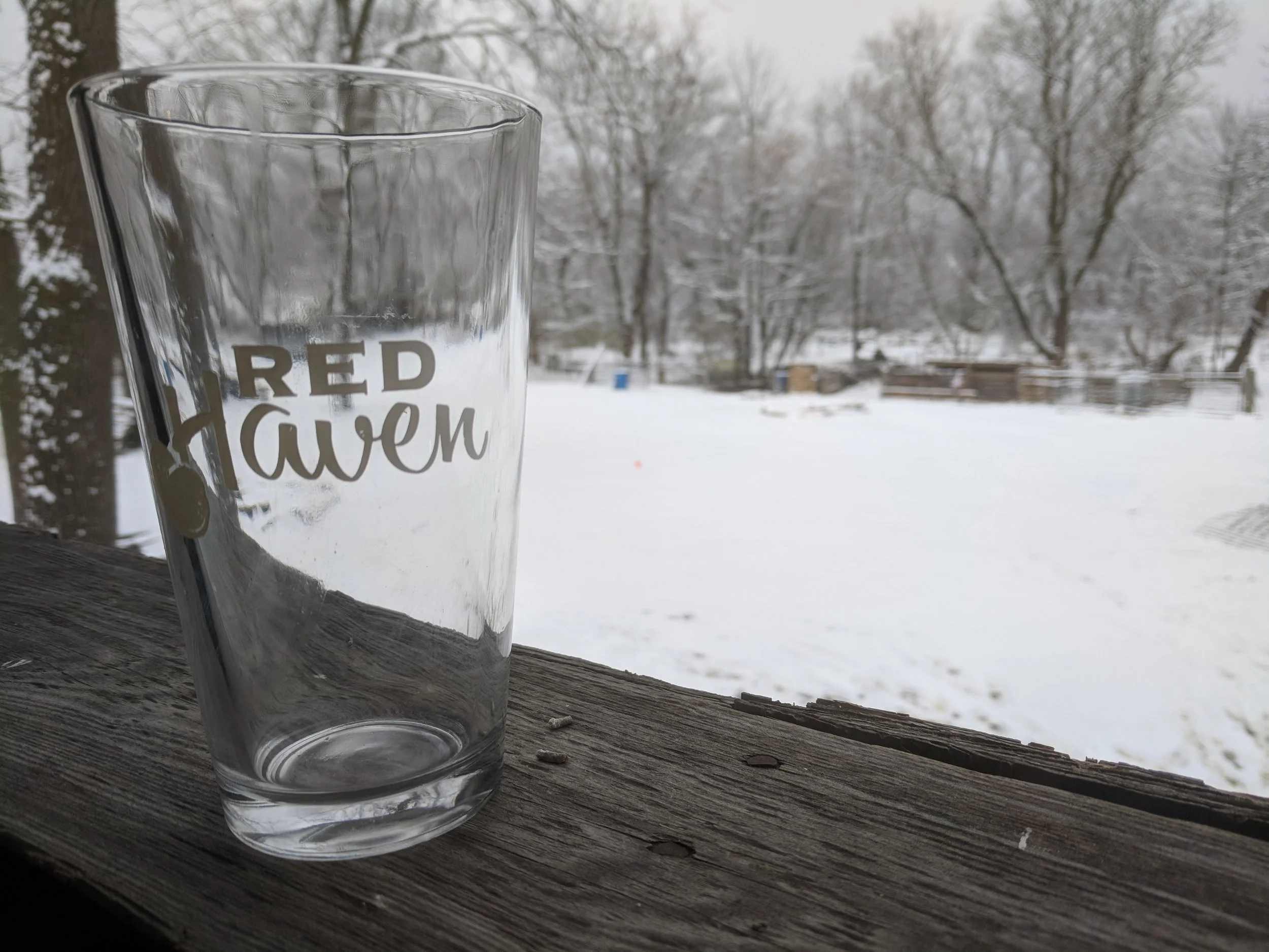 Empty glass with "Red Haven" logo on a snowy balcony, trees in the background.