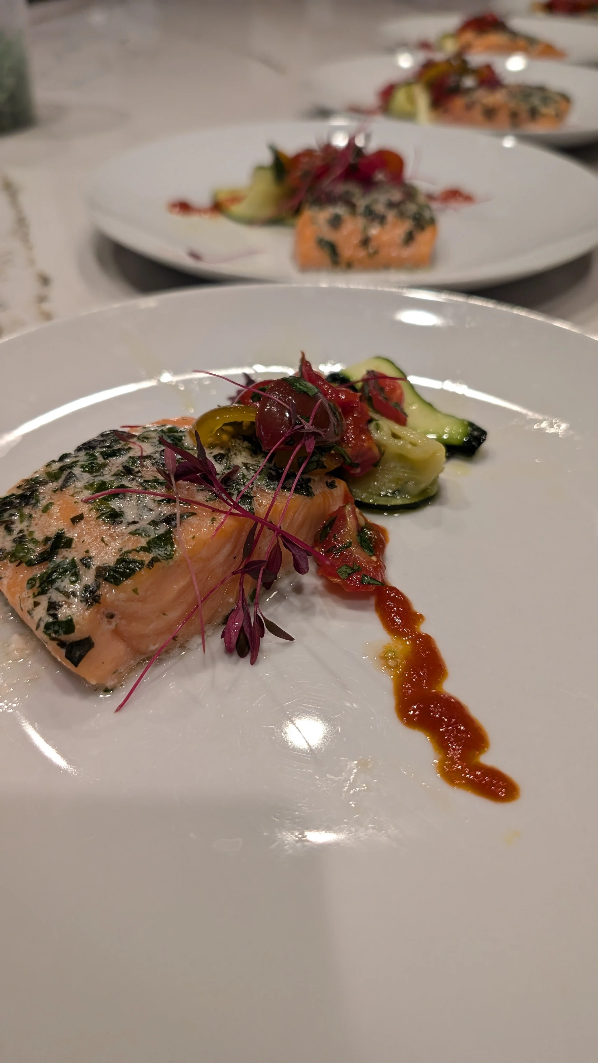 Plated salmon dish with herbs, zucchini, cherry tomatoes, and garnish on a white plate.