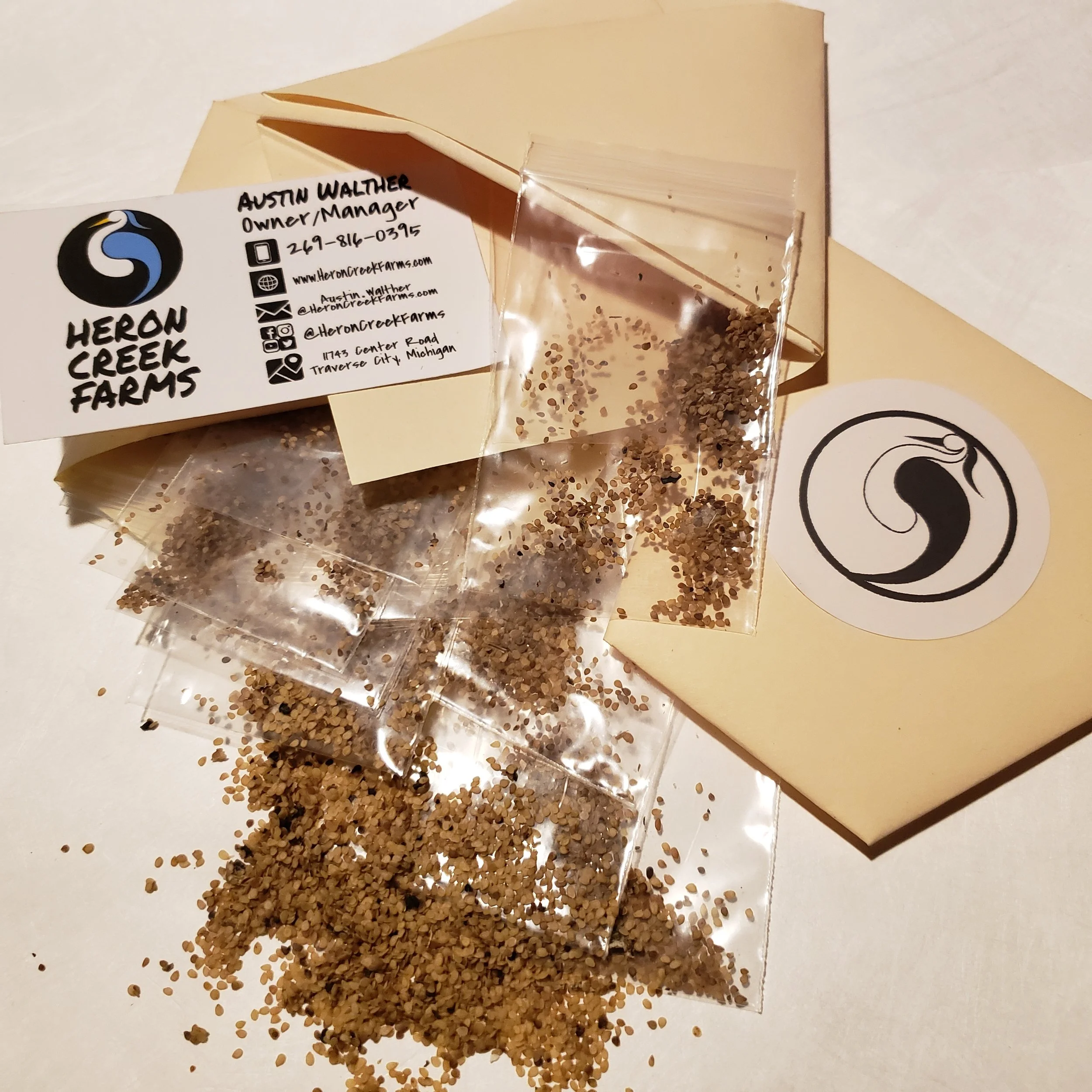 Packets of seeds spilled from envelopes, with a business card reading 'Heron Creek Farms' and contact information.