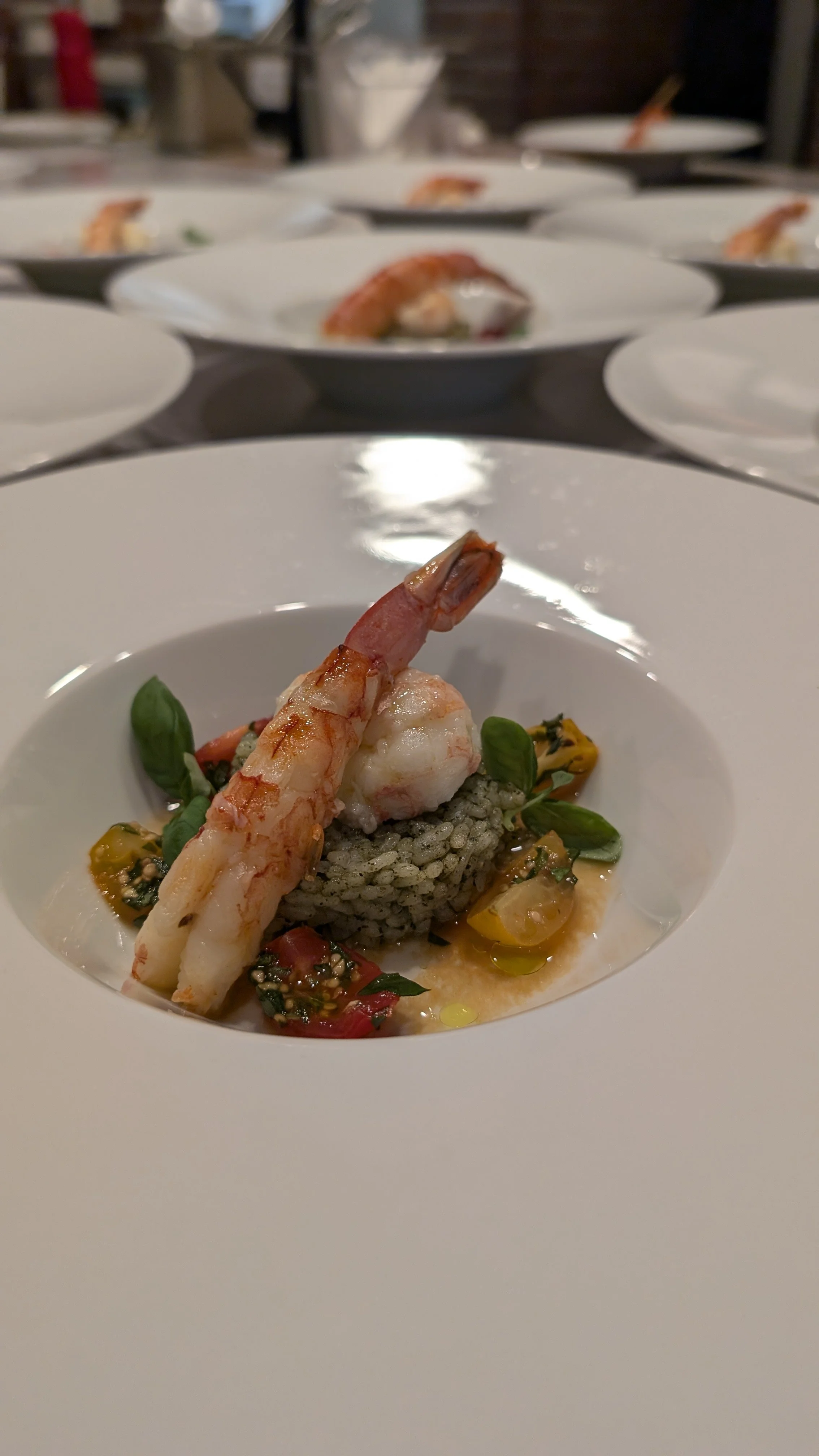 Gourmet dish with shrimp on green rice, garnished with herbs and cherry tomatoes.