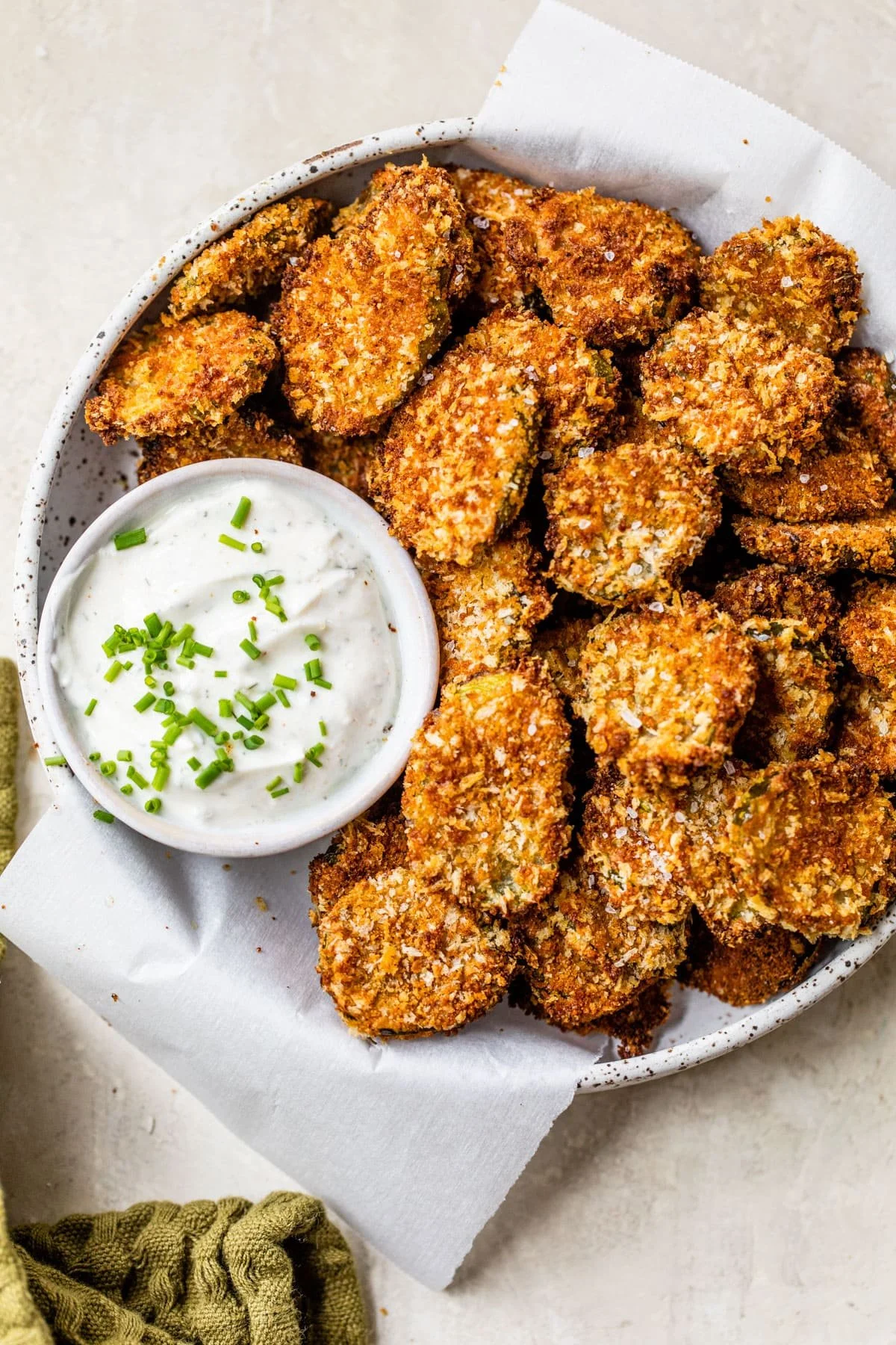 Plate of crispy fried pickles with a side of ranch dipping sauce garnished with chives.