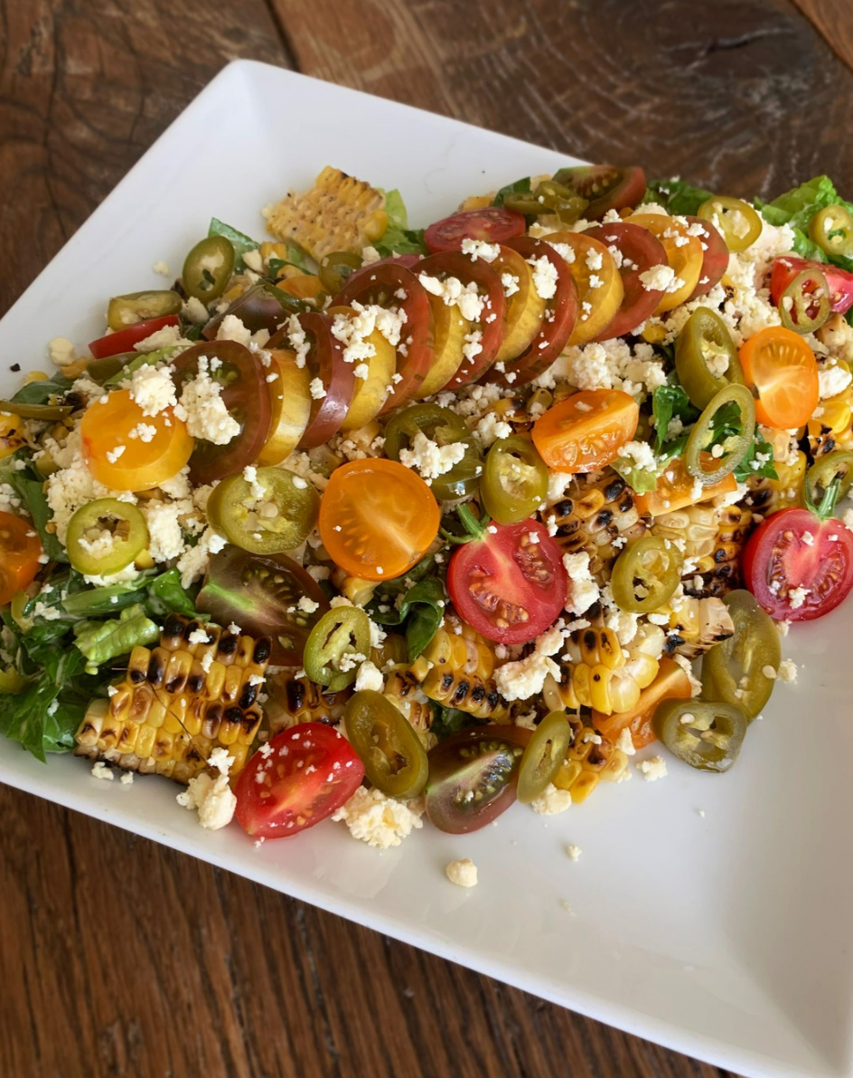 Grilled corn salad with cherry tomatoes, jalapeños, and cheese on a white plate.
