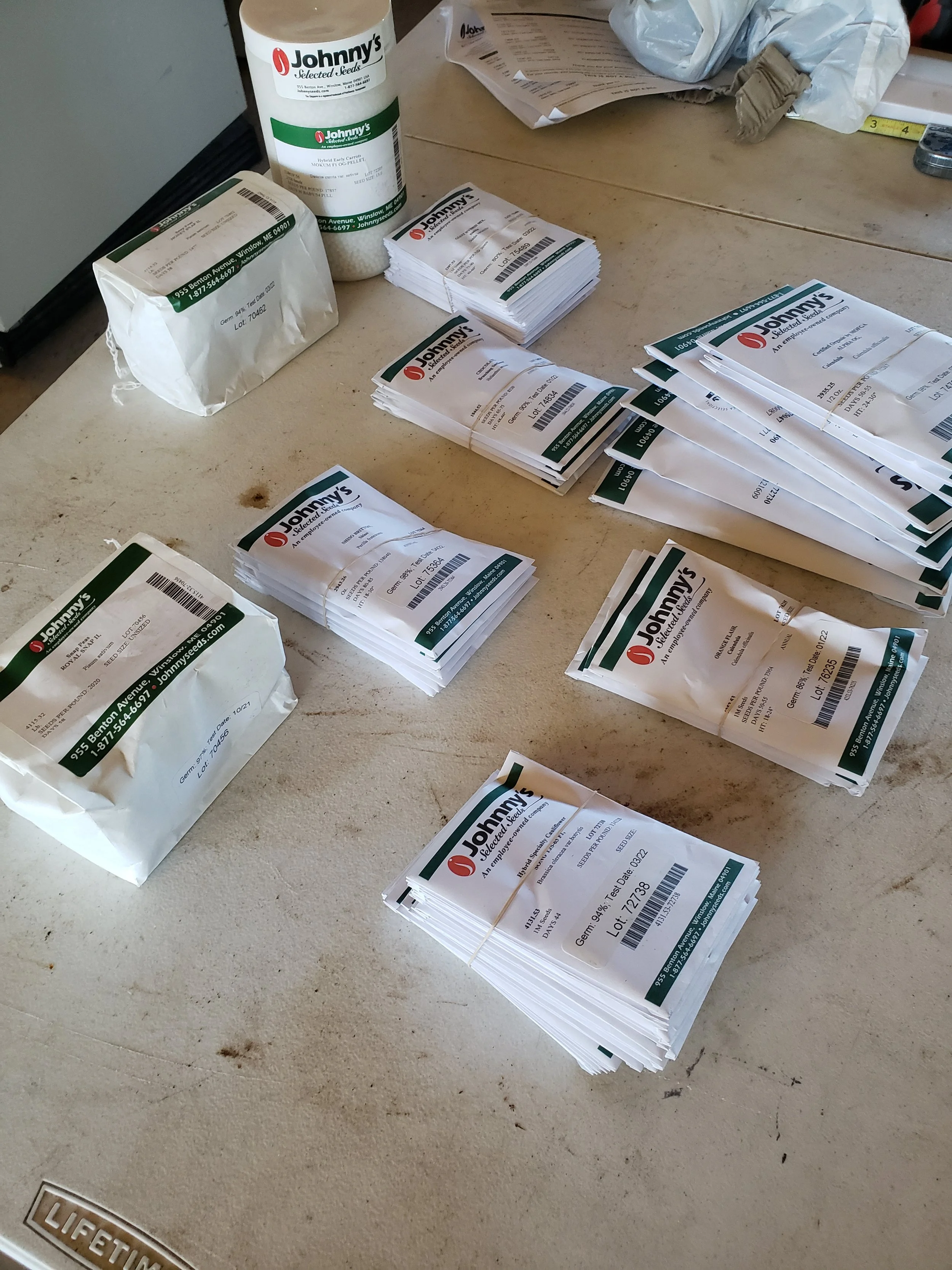 Packets and bags of seeds from Johnny's Selected Seeds arranged on a table.