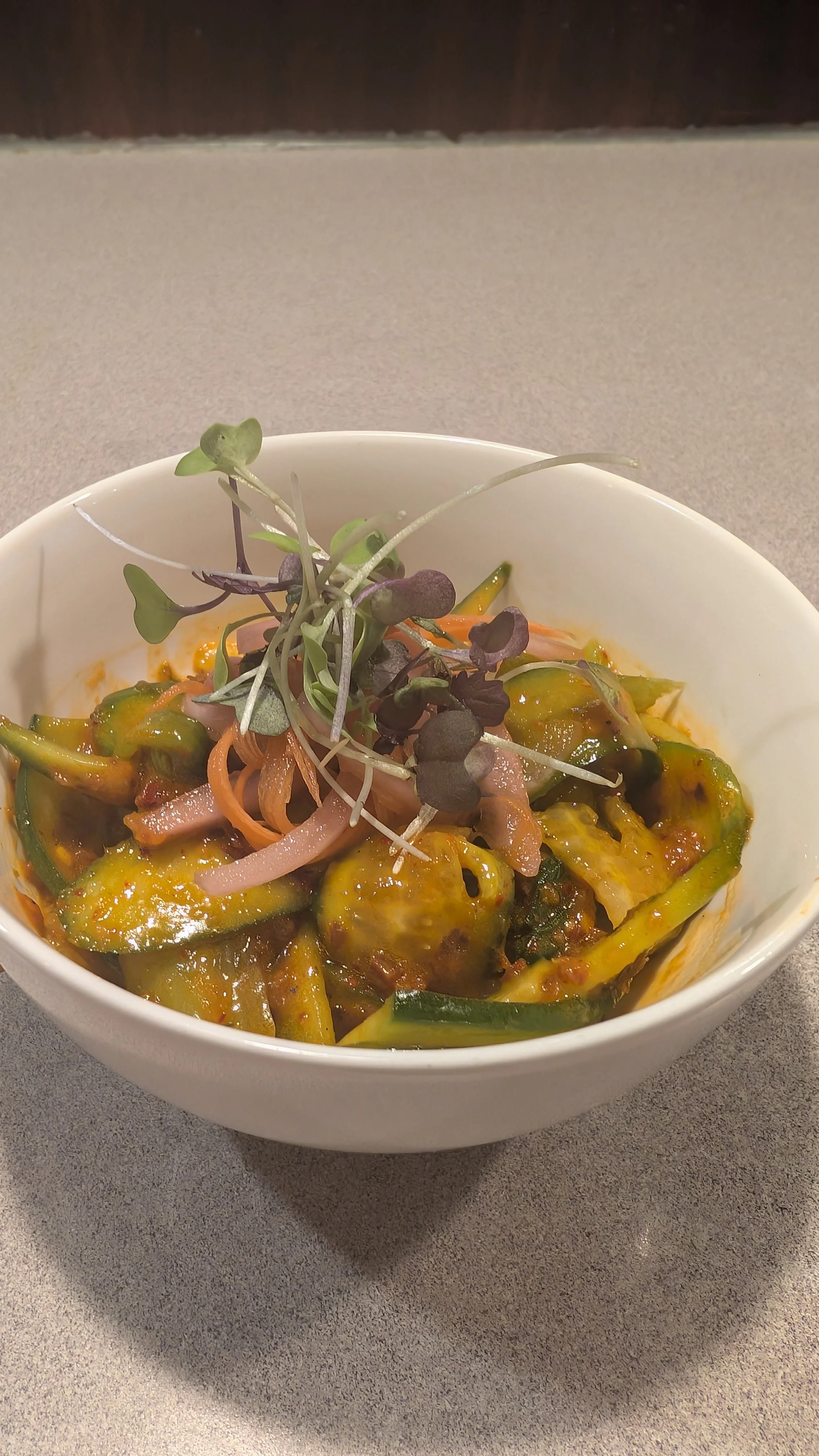 Bowl of sautéed vegetables with sauce and microgreens garnish.
