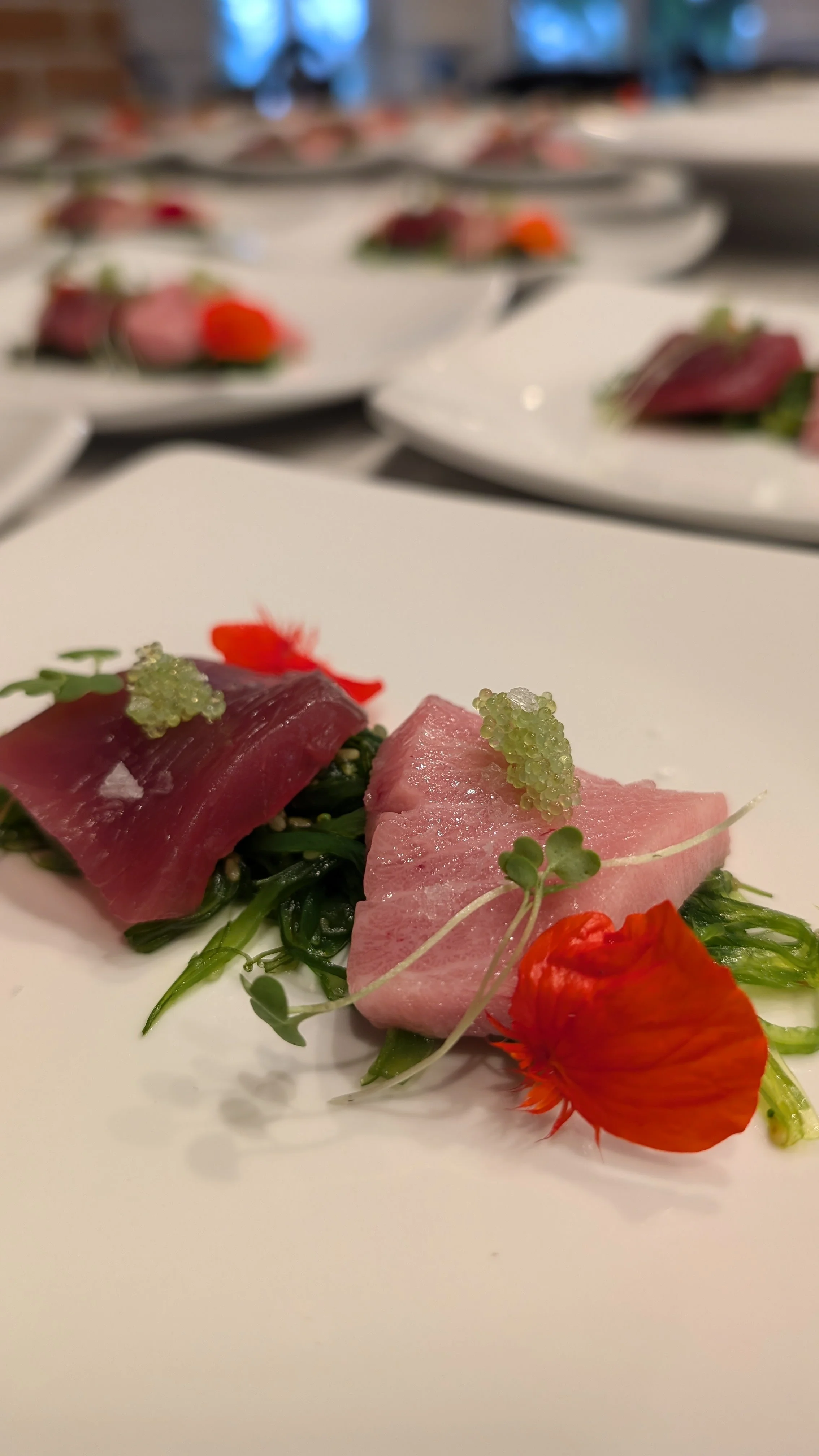 Plate of sushi featuring sliced tuna with seaweed salad, garnished with green caviar and an edible flower.