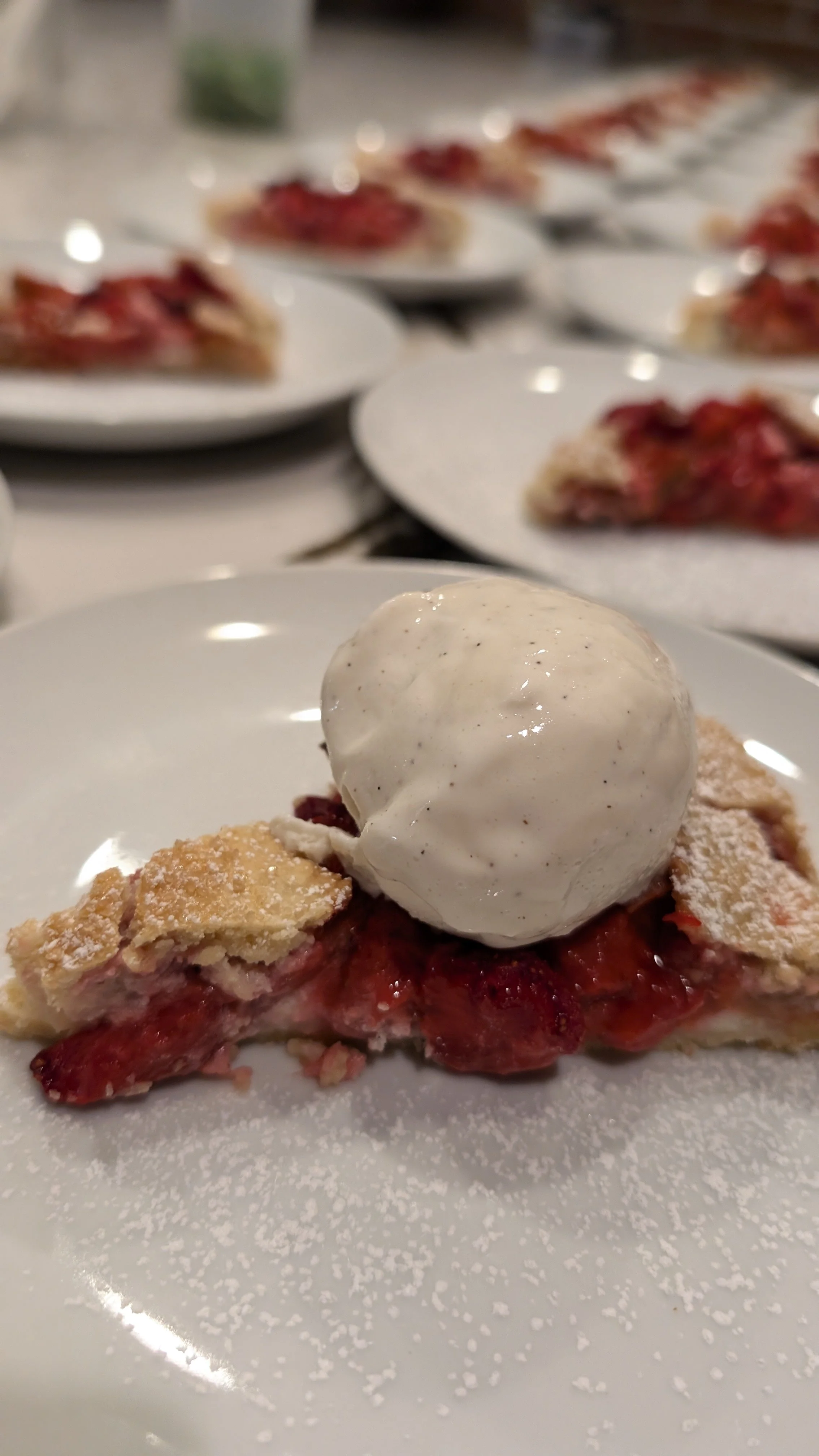 Slice of strawberry pie topped with a scoop of vanilla ice cream on a white plate.