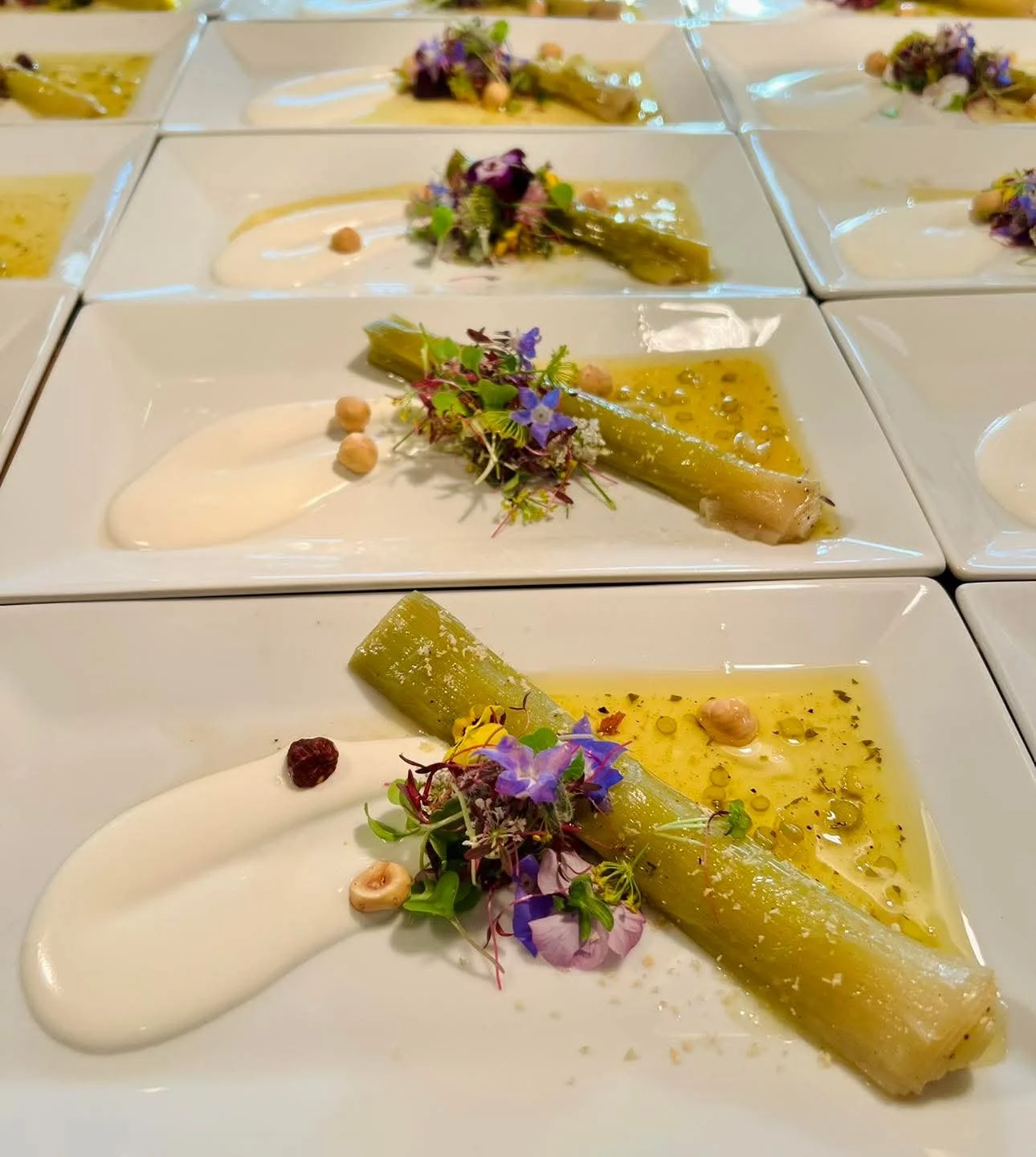 Plates of gourmet appetizers with leeks, creamy sauce, edible flowers, and nuts.