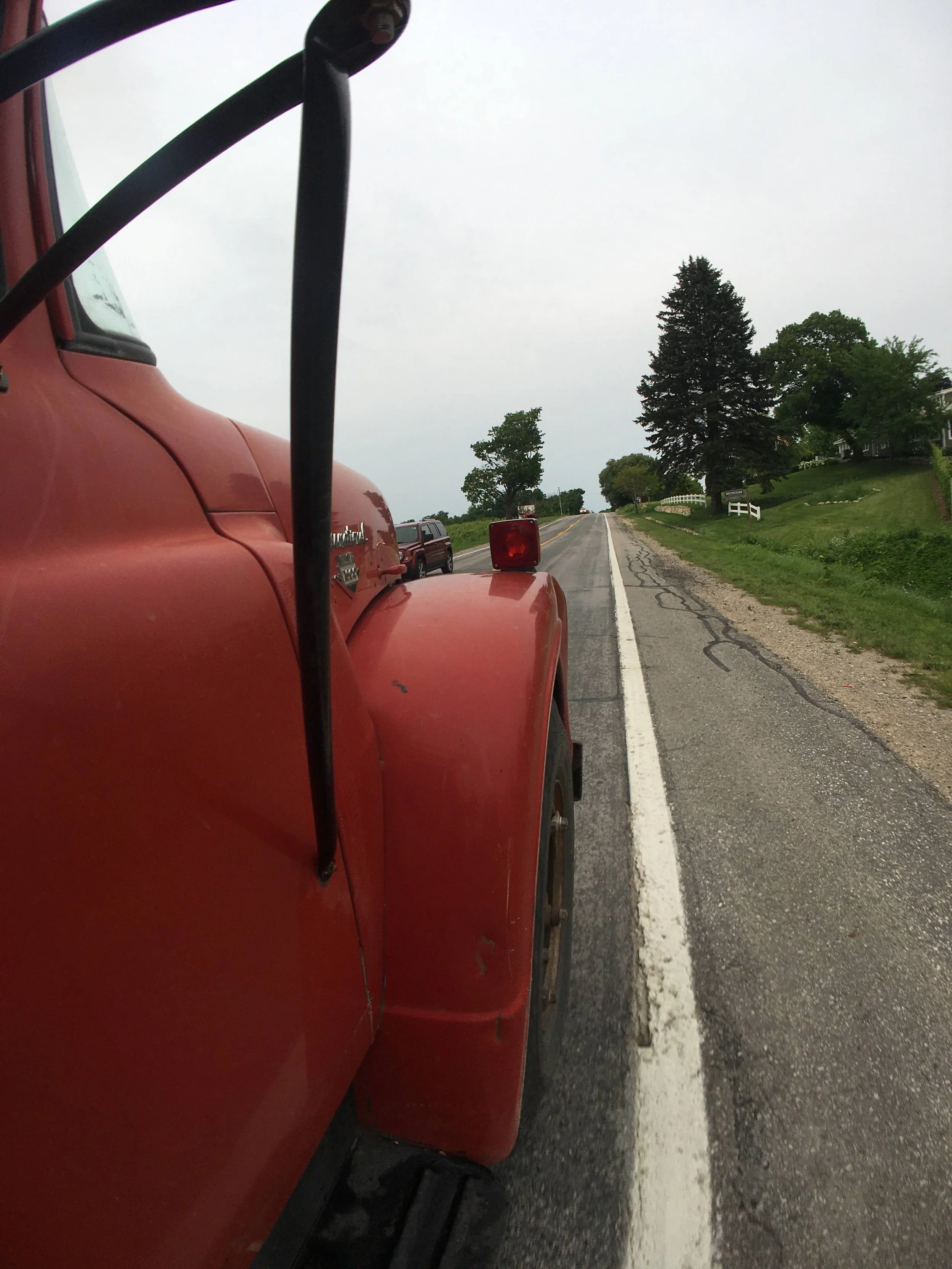 Red vintage truck on a rural road with trees and fields.