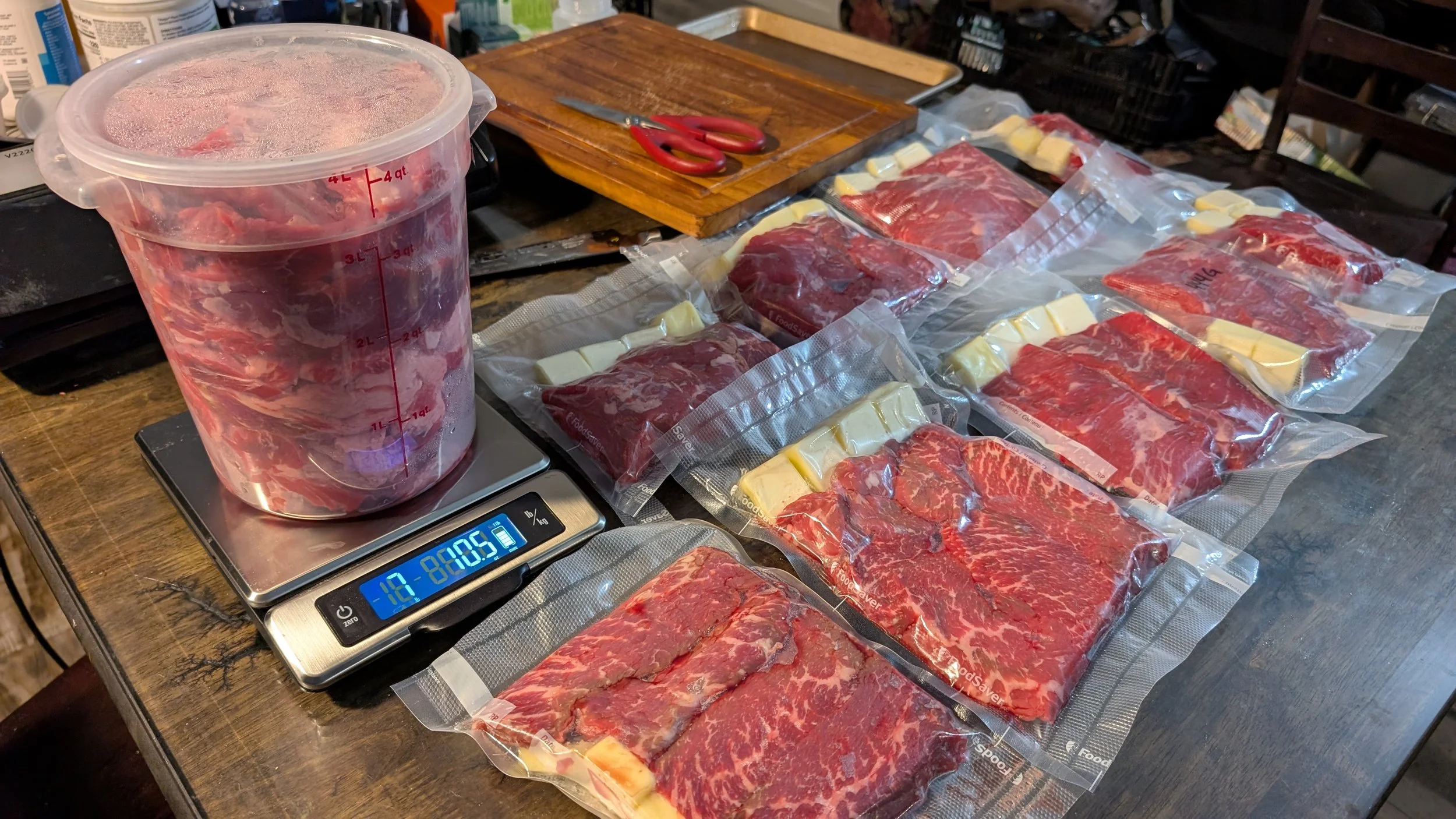 Vacuum-sealed packages of raw beef and cheese on a table, with a large container of meat on a digital scale.