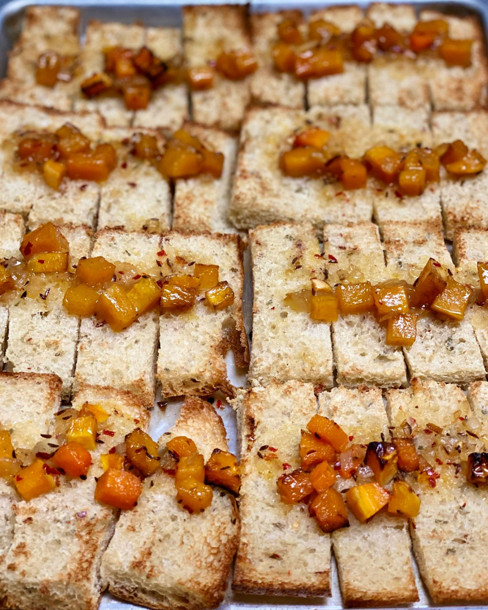 Toasted bread slices topped with diced caramelized vegetables on a baking tray.