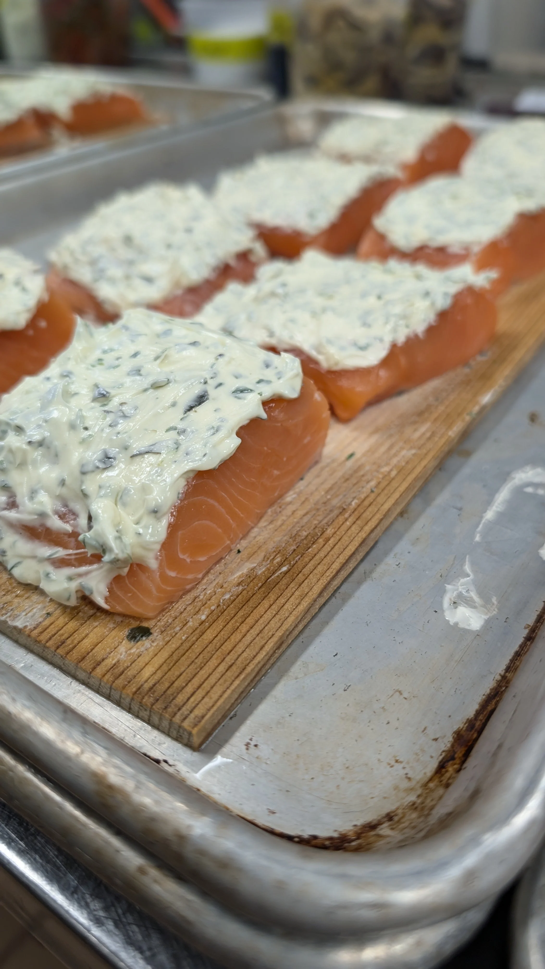 Raw salmon fillets with creamy sauce on cedar planks on a baking sheet.
