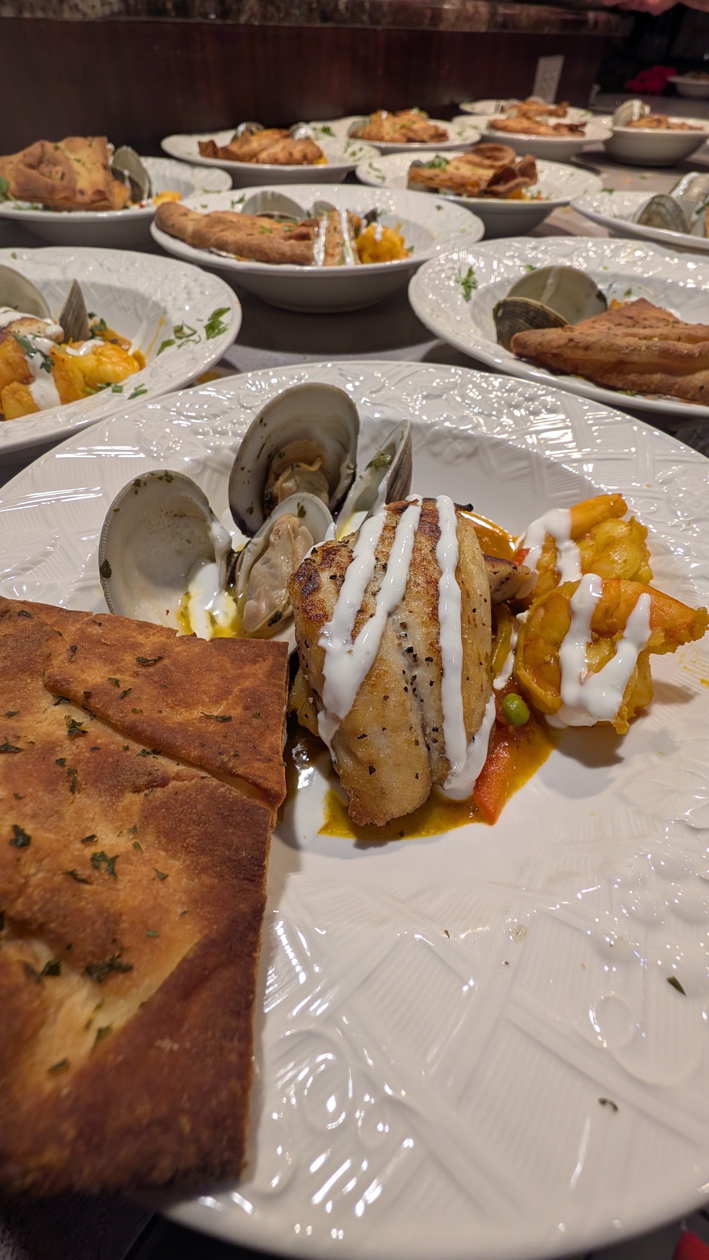 Plates of seafood dish with clams, fish, shrimp, sauce, and flatbread garnish