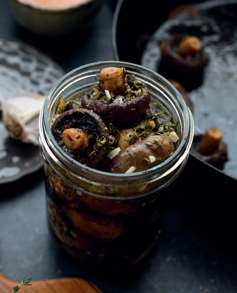 Jar of marinated mushrooms with herbs and garlic on a dark background.