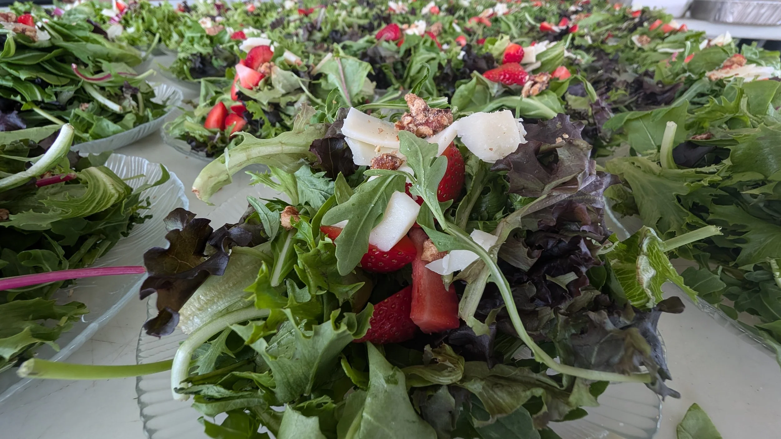 Fresh salad with mixed greens, strawberries, cheese, and nuts on plates.