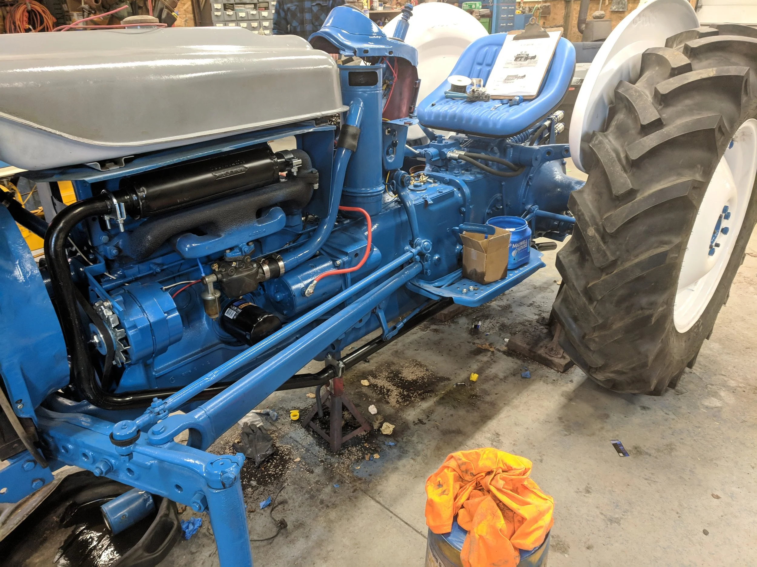 A partially disassembled blue tractor undergoing maintenance in a workshop with large rear wheel and visible engine components.