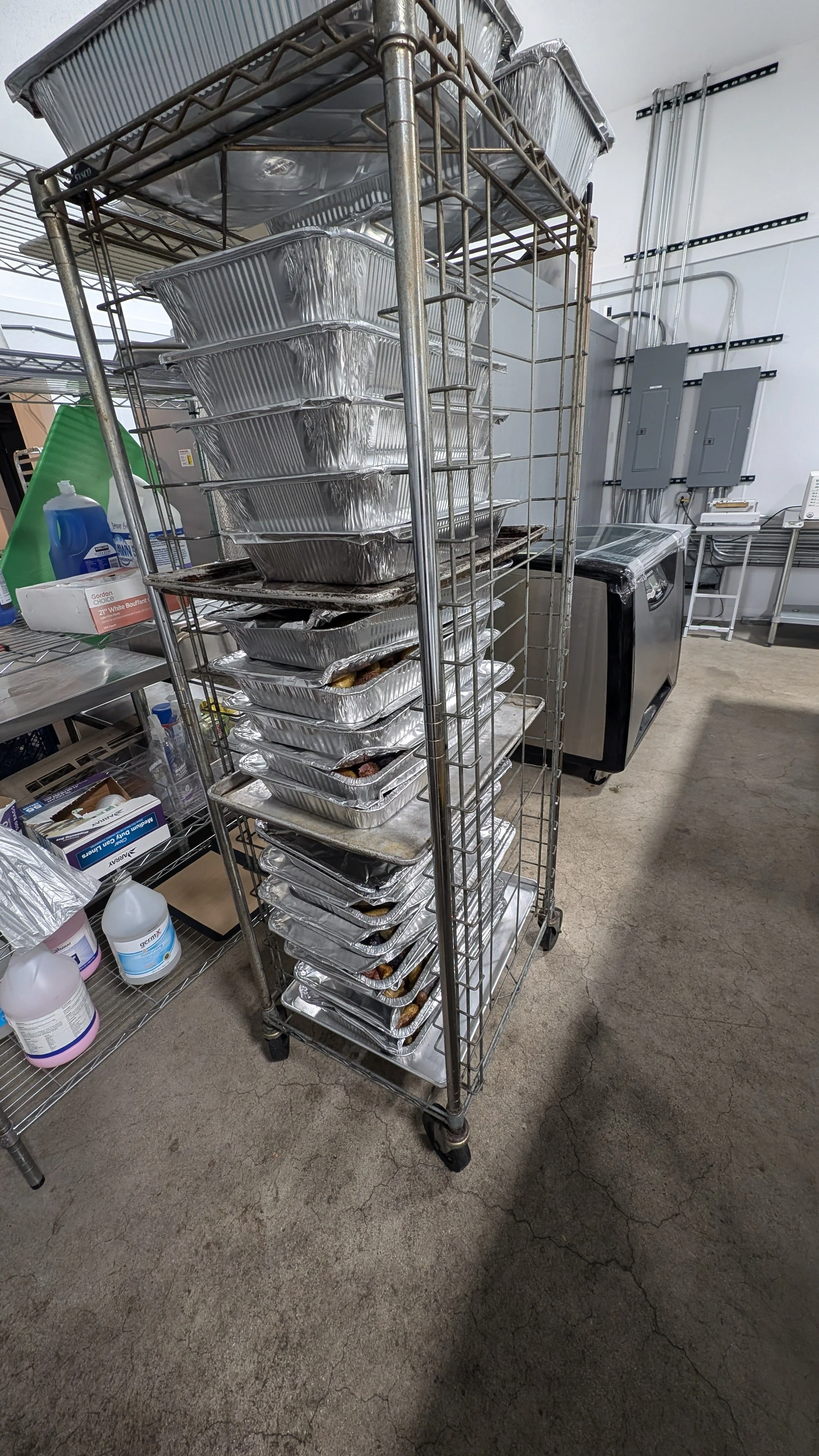 Metal rack with stacked aluminum trays in an industrial kitchen setting.