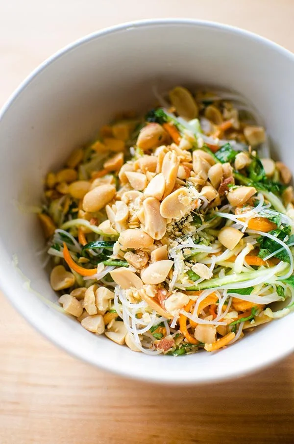 A bowl of Thai-style noodle salad with peanuts, carrots, zucchini, and fresh greens.