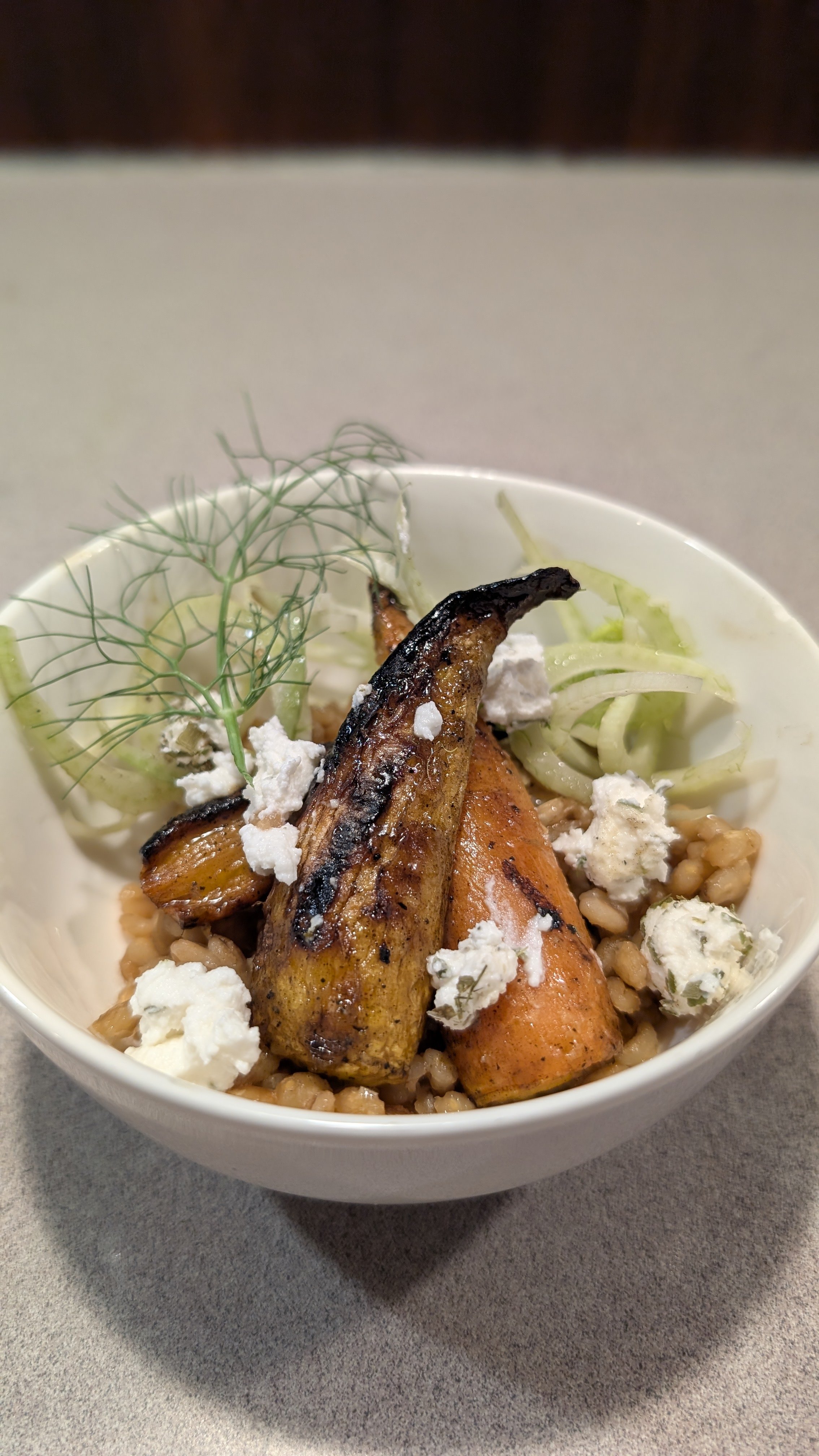 A bowl of roasted carrots and grains topped with crumbled cheese and garnished with fresh dill.