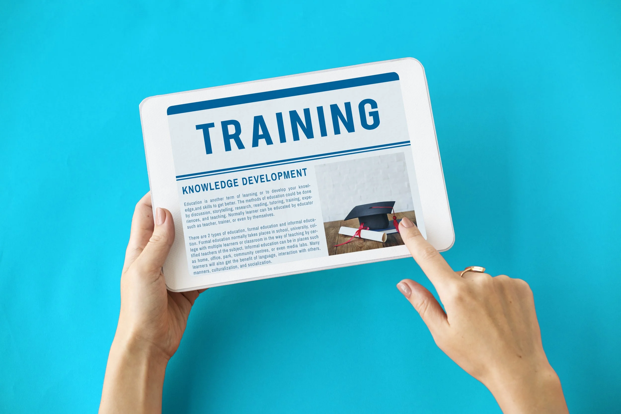 Eine Person hält ein Tablet mit einer Seite über Schulungen und Wissenentwicklung, auf dem Bild ist auch ein Abschlusskappe sichtbar.