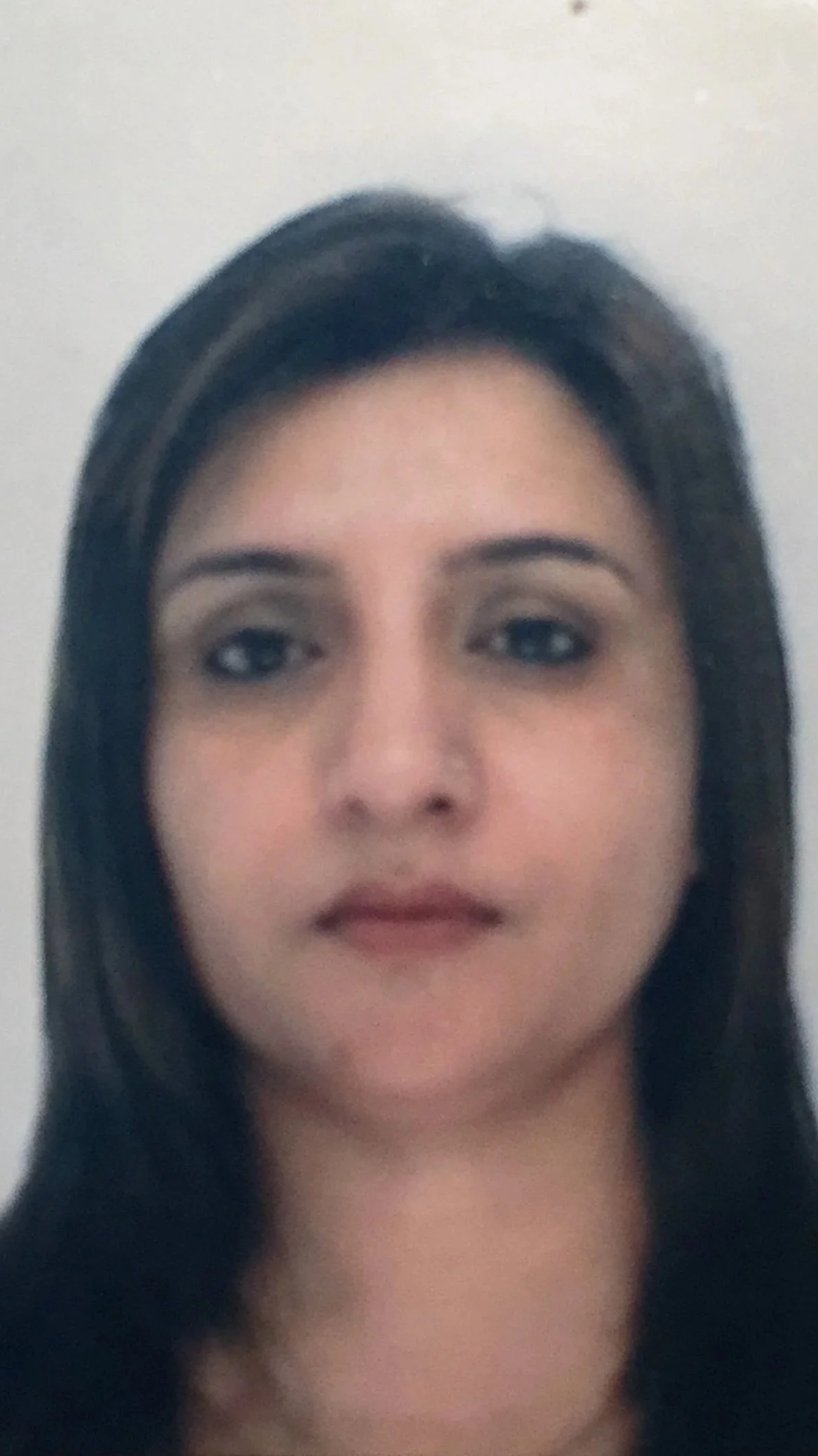 Close-up of a woman's face with dark hair and neutral expression against a plain background.