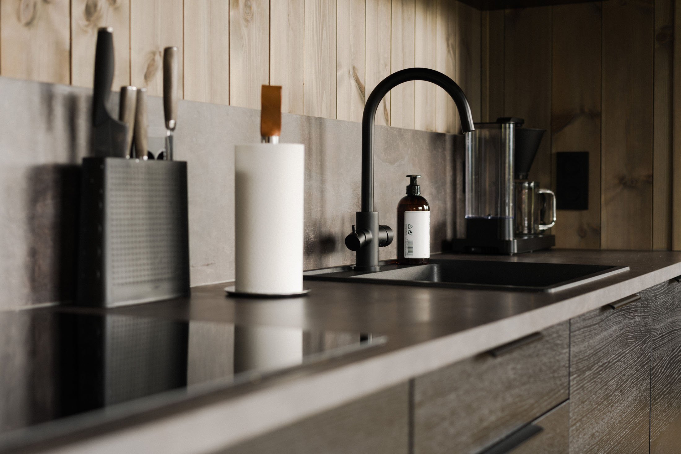 Modern kitchen countertop with knife block, paper towel holder, black faucet, soap dispenser, and coffee maker.
