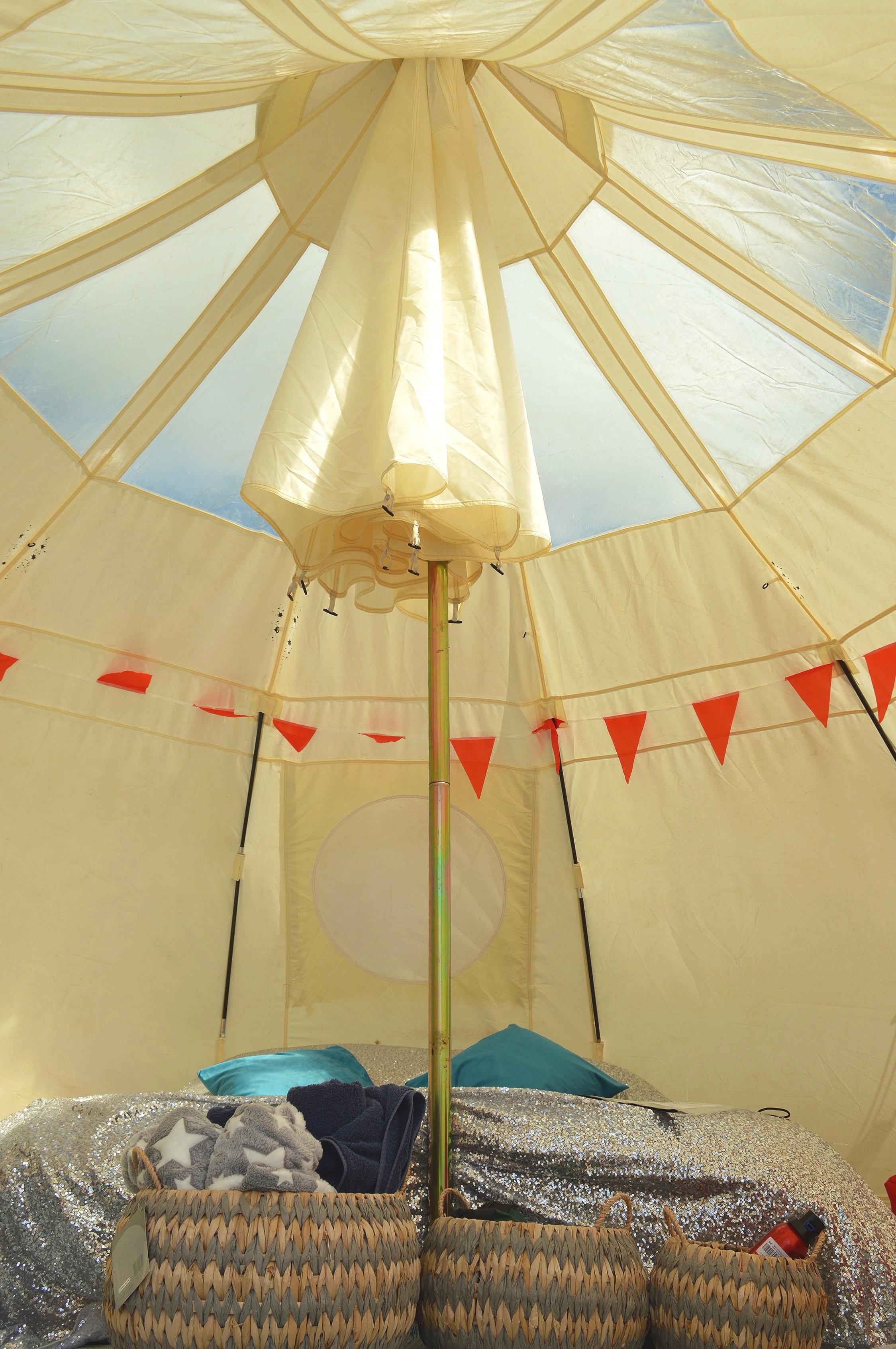 Interior of star gazing tent with a central pole, decorated with red triangular pennant flags, woven baskets, bedding, and pillows.