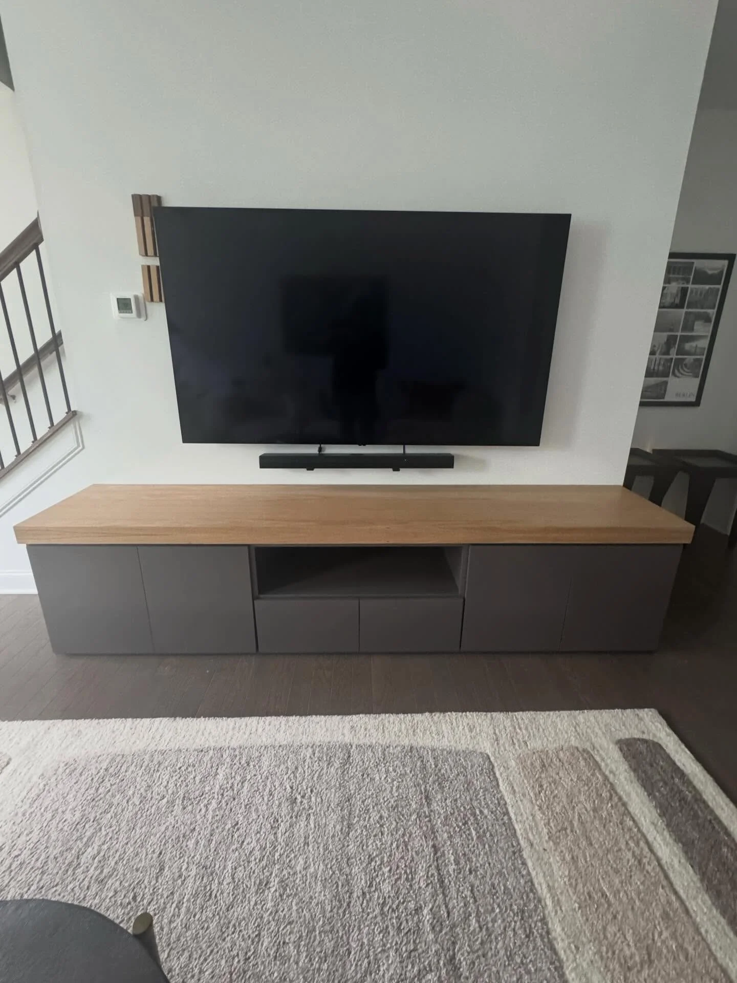 The cabinet is a long, low-profile custom media console with a modern, minimalist design.

It features a thick natural wood countertop that runs the entire length of the cabinet, creating a warm contrast with the darker base. The wood top appears sol