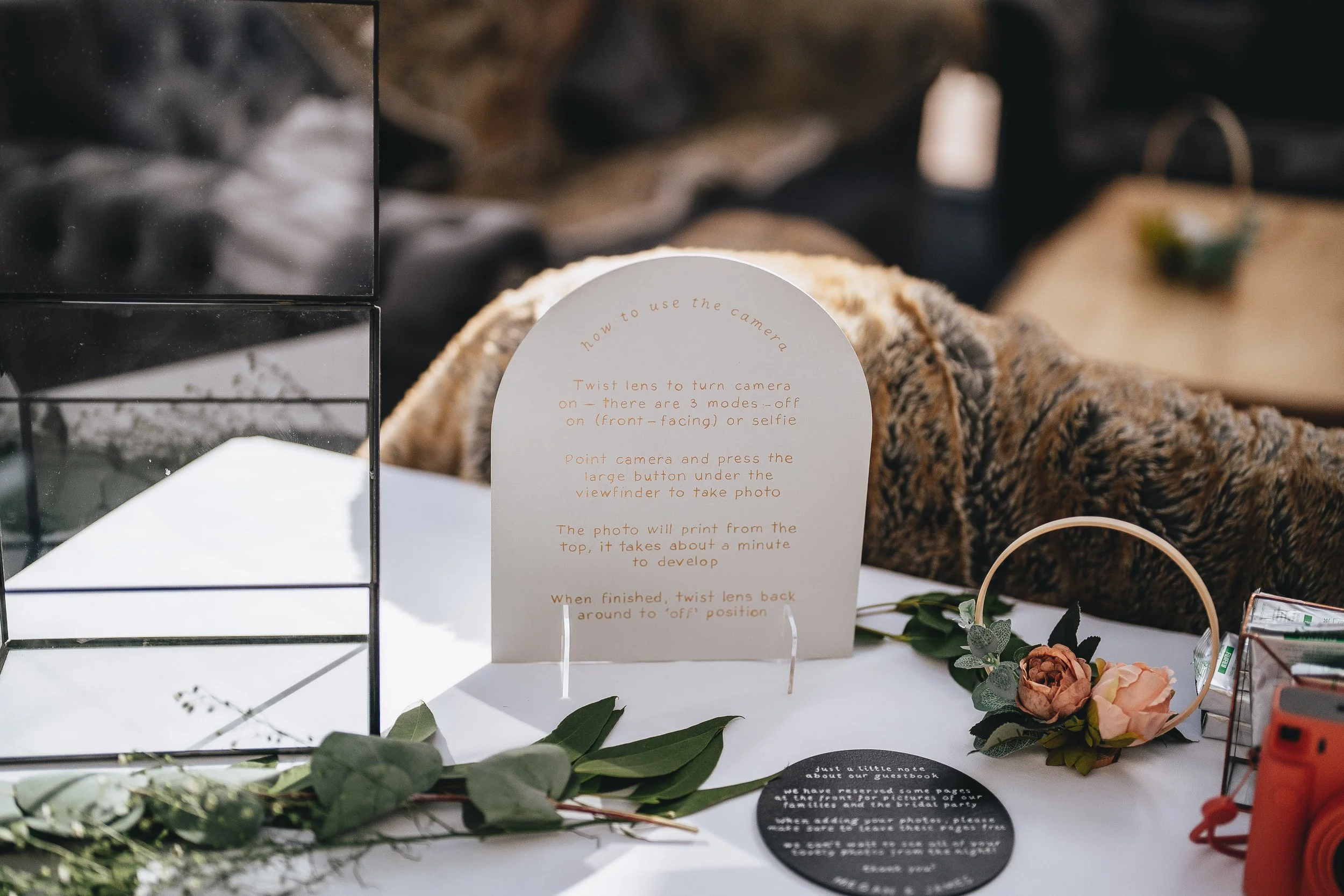 Instruction sign on a table with flowers and photo props, explaining how to use a camera to take photos at an event.
