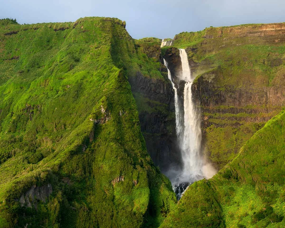 A lush green valley with a large waterfall cascading down a cliff surrounded by verdant hills.